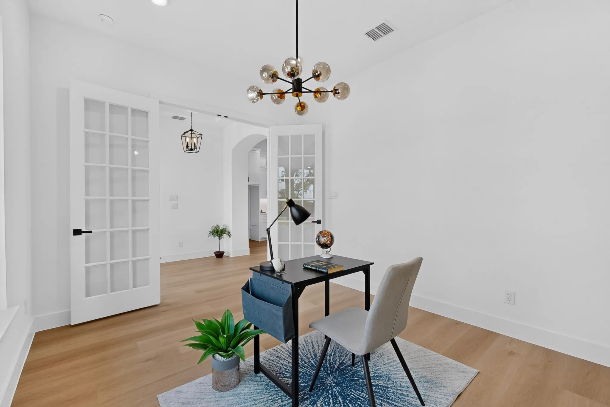 Bright interior space featuring wood-finish flooring, white walls, and a contemporary chandelier