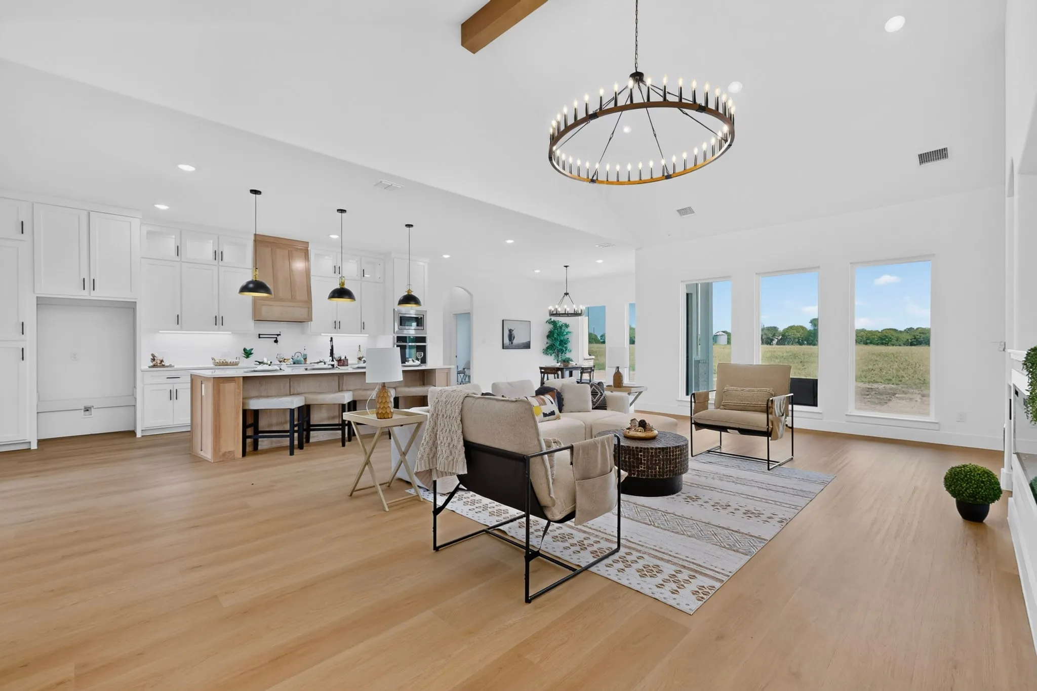 Open-concept living space featuring high vaulted ceilings with an exposed wood beam, natural wood-finish flooring, and a contemporary chandelier
