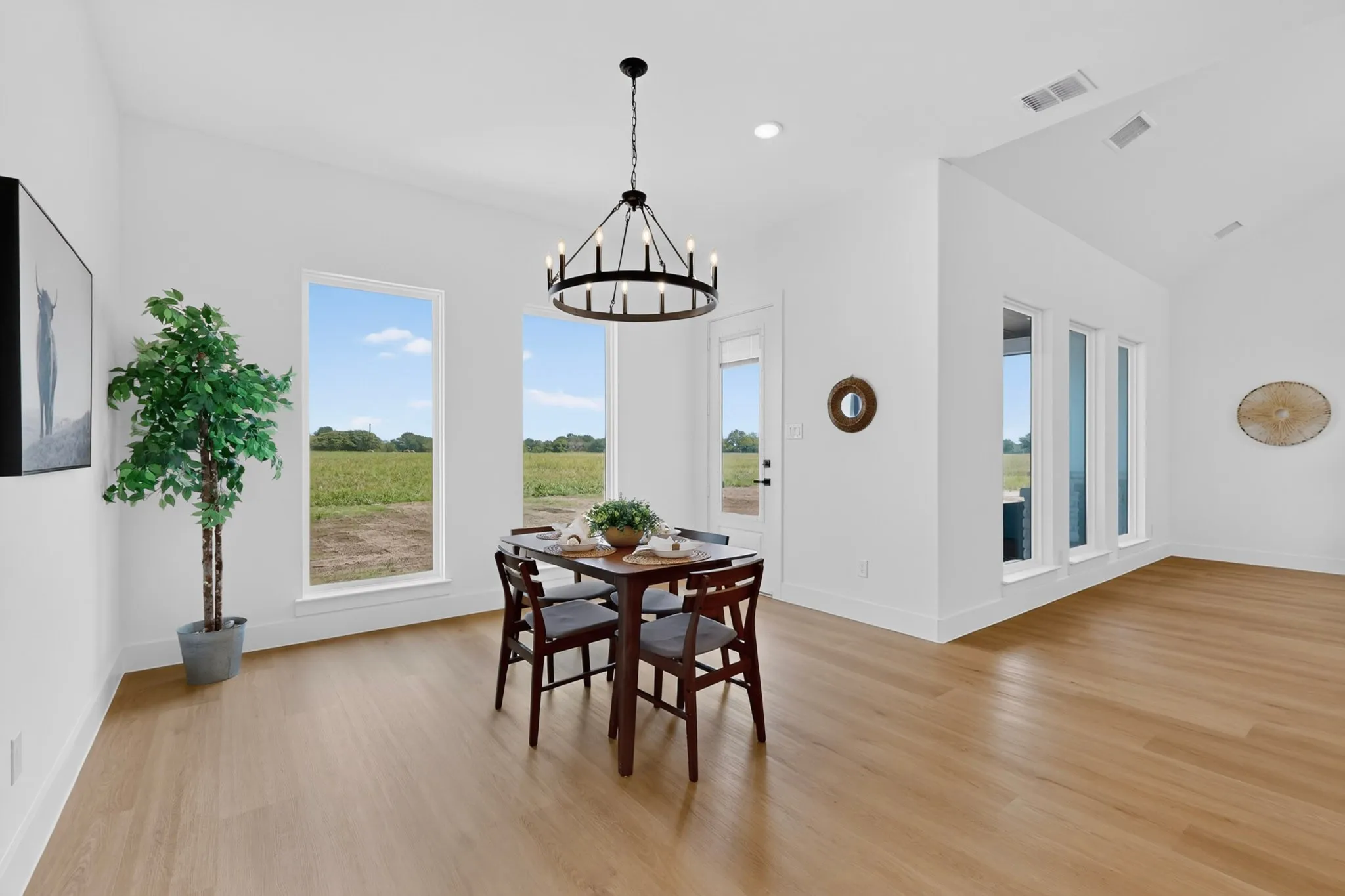 Spacious room featuring wood-finish flooring, white walls, and a contemporary chandelier