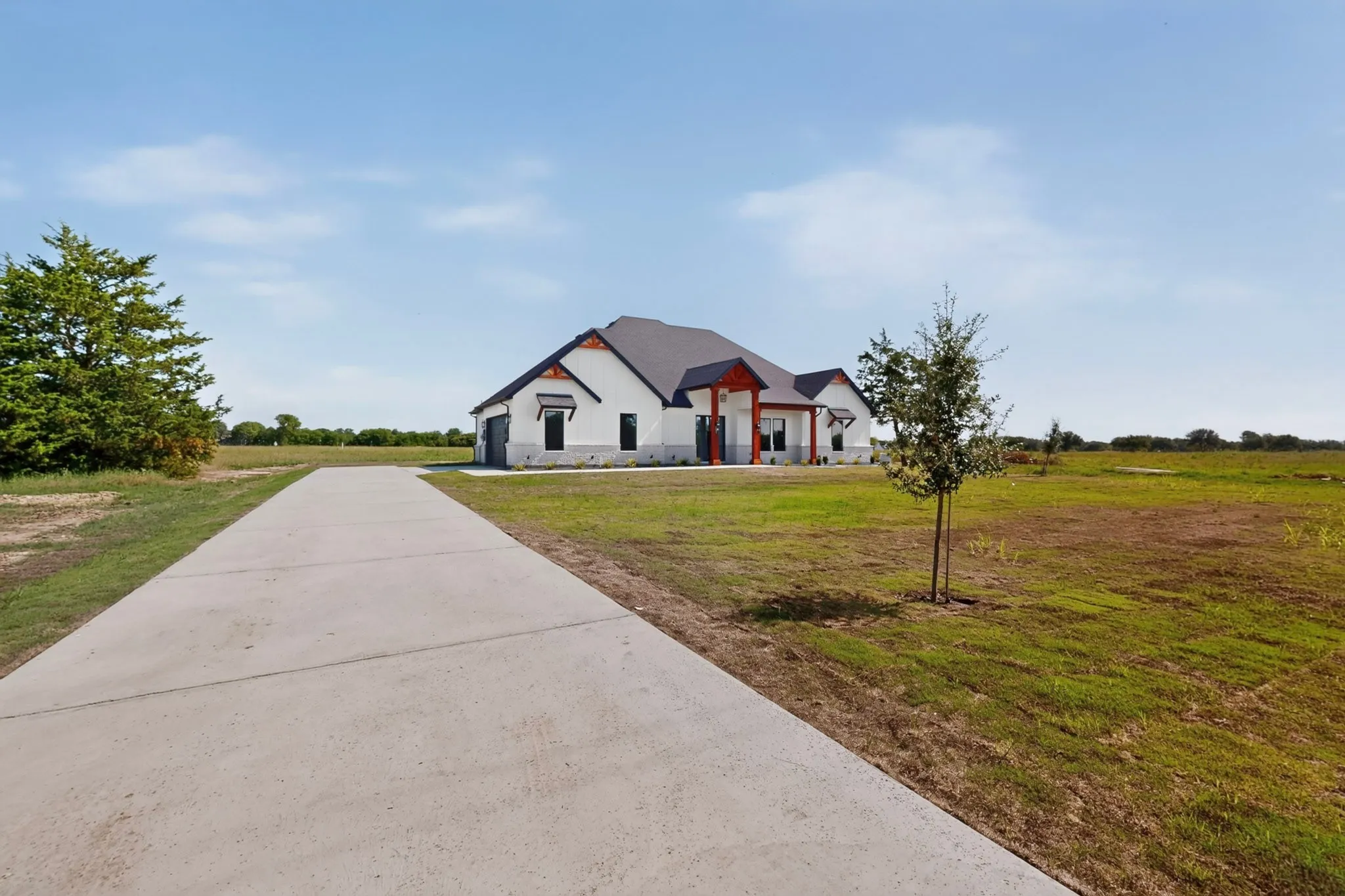 Concrete driveway extending towards a white exterior home with a dark roof