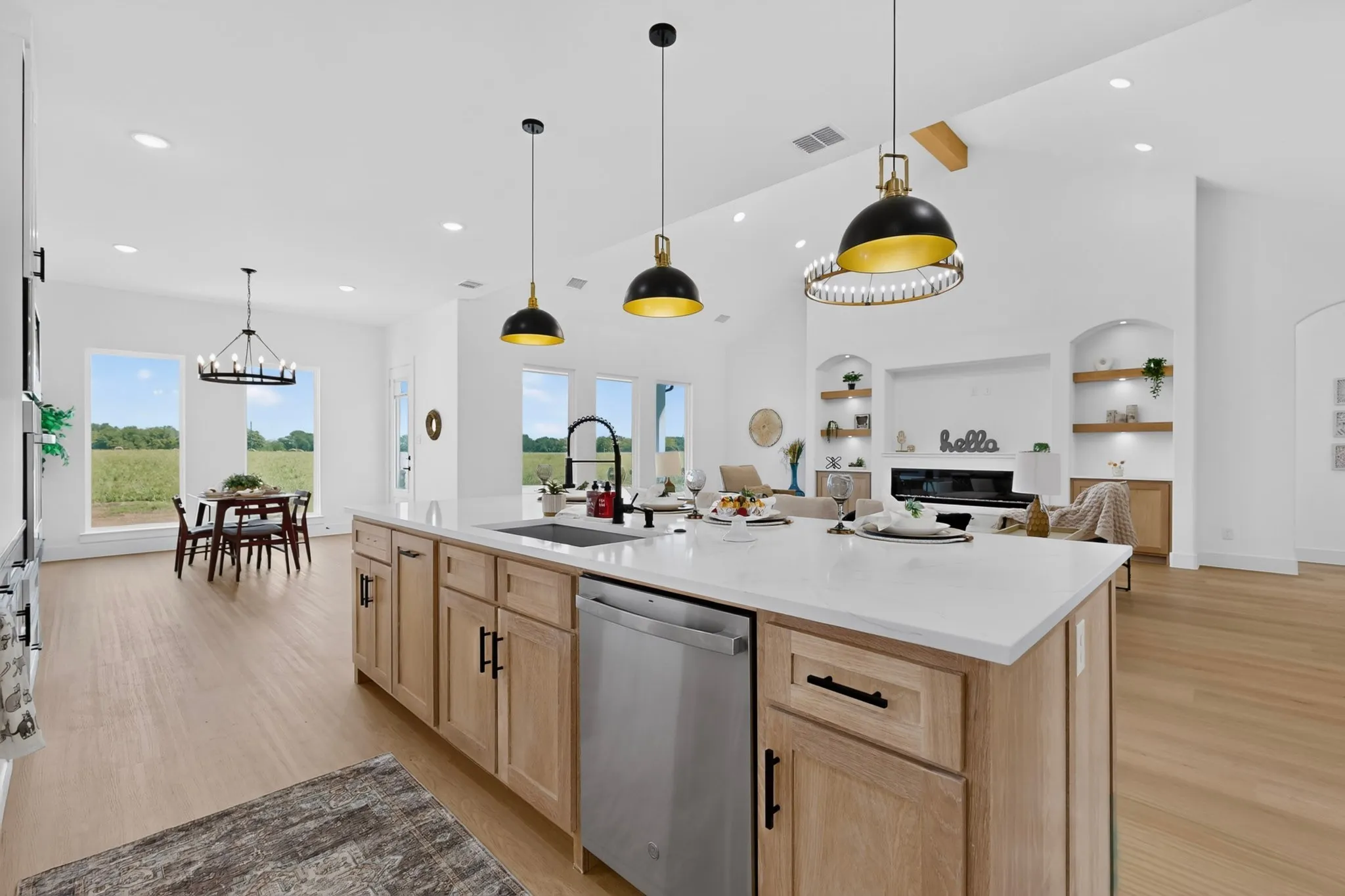 Open-concept living space featuring a central kitchen island with a white countertop and natural wood-finish cabinetry, a stainless steel dishwasher, and contemporary pendant lighting