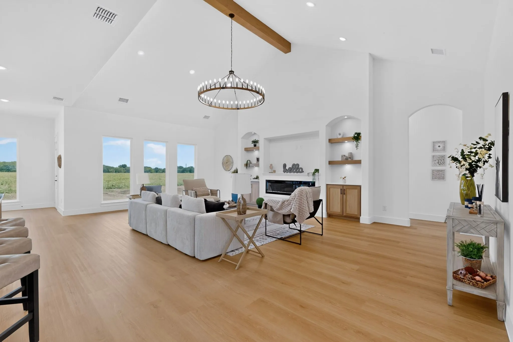 Spacious living area featuring light wood-finish flooring, vaulted ceilings with a prominent exposed beam, a contemporary chandelier, and recessed lighting
