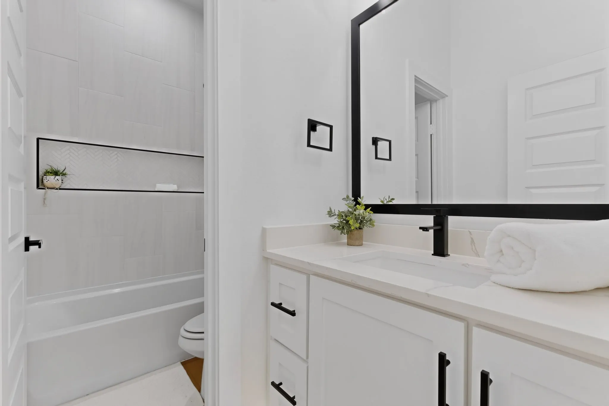 Bathroom featuring a single vanity with a white countertop and integrated sink, matte black faucet, and a large black-framed mirror