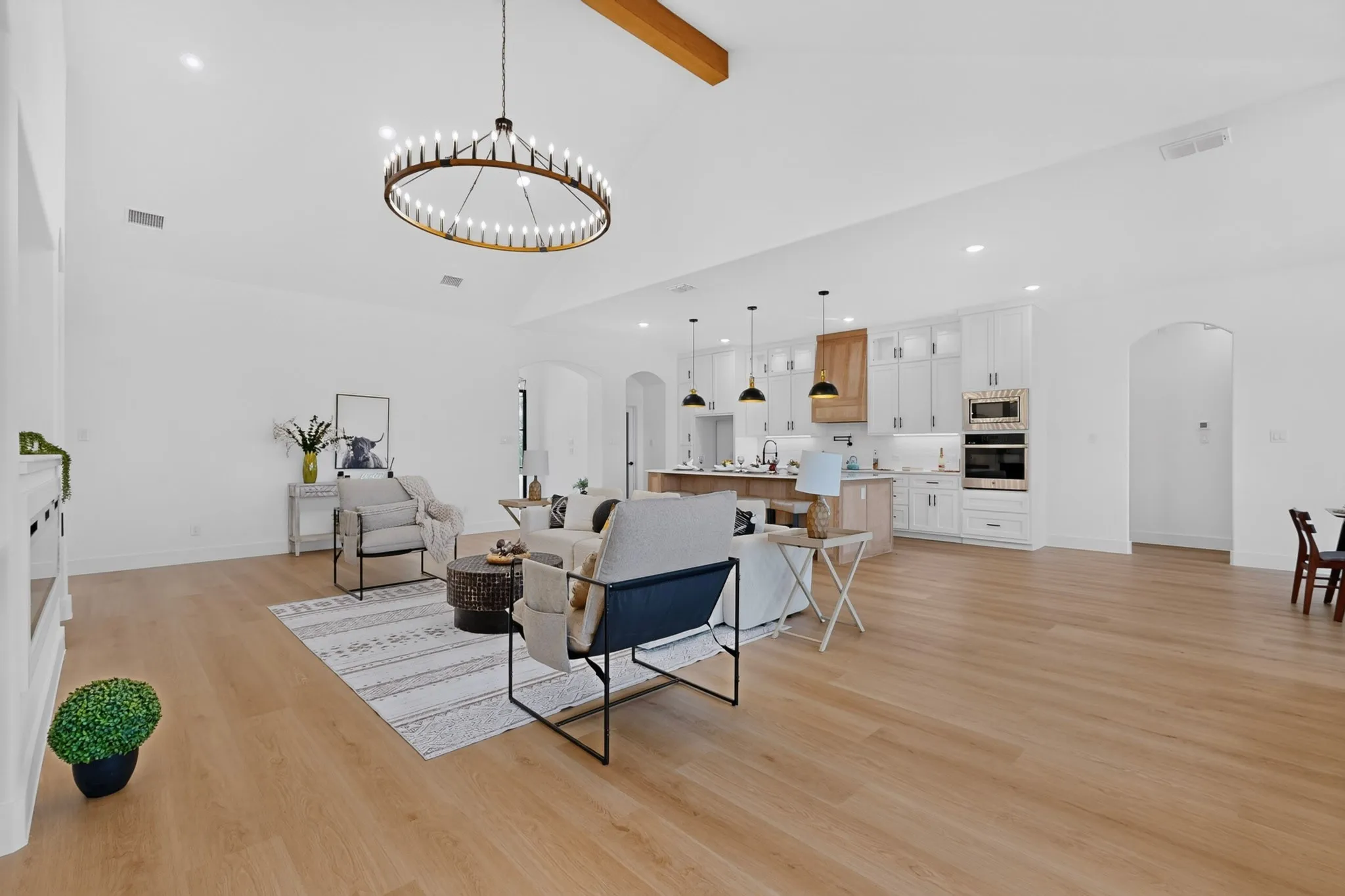 Open-concept living area featuring wood-finish flooring, a vaulted ceiling with exposed beam, and a large circular​​‌​​​​‌​​‌‌​‌‌​​​‌‌​‌​‌​‌​​​‌​​ chandelier