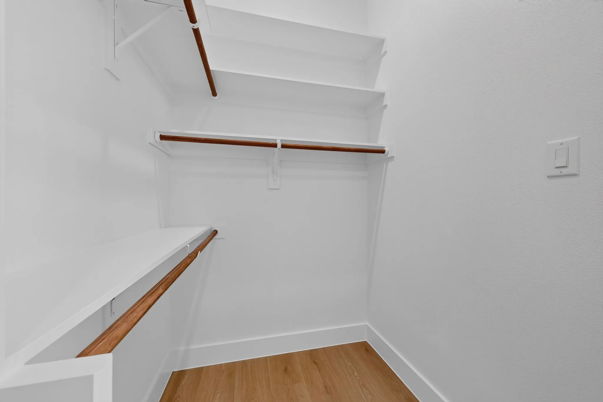 Walk-in closet featuring built-in shelving, wood-finish hanging rods, white baseboards, and wood-finish flooring