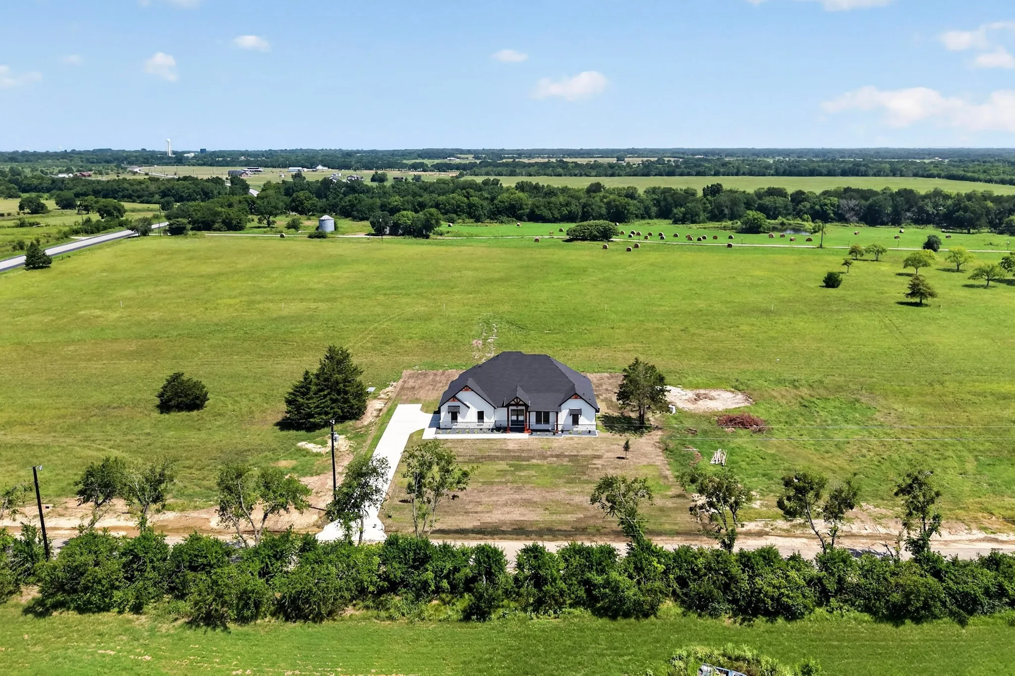 Expansive verdant landscape surrounding a newly constructed home with a dark roof