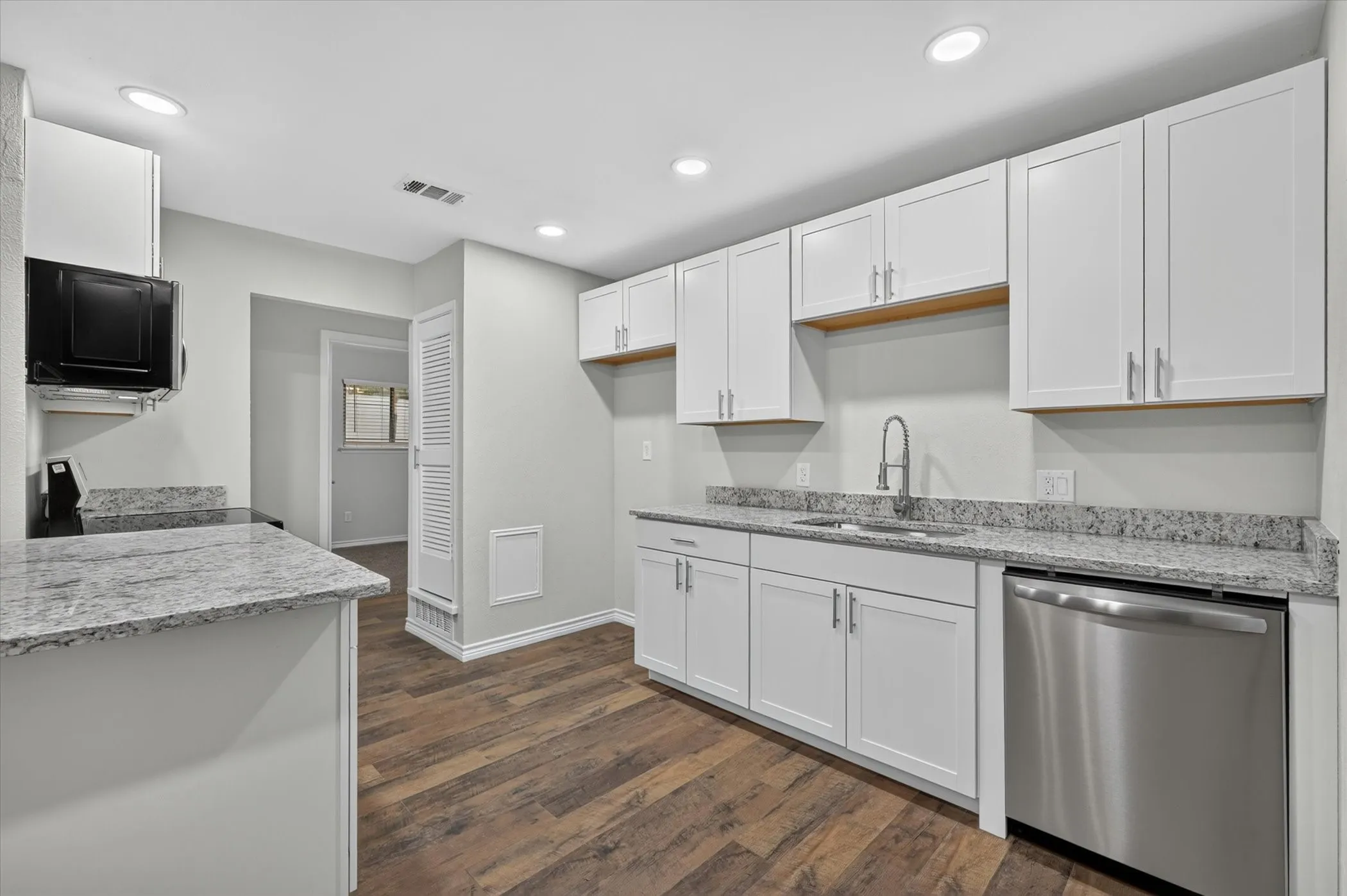 Modern kitchen featuring white shaker cabinetry, stainless steel dishwasher, wood-finish flooring, recessed lighting, and speckled countertops