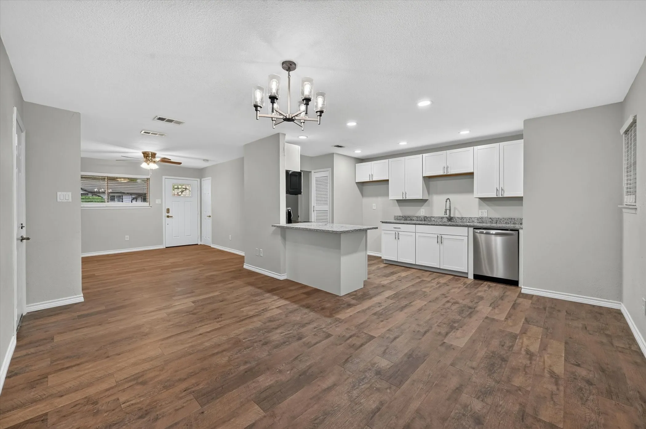 Open-concept living area and kitchen featuring wood-finish flooring, recessed lighting, and a modern chandelier