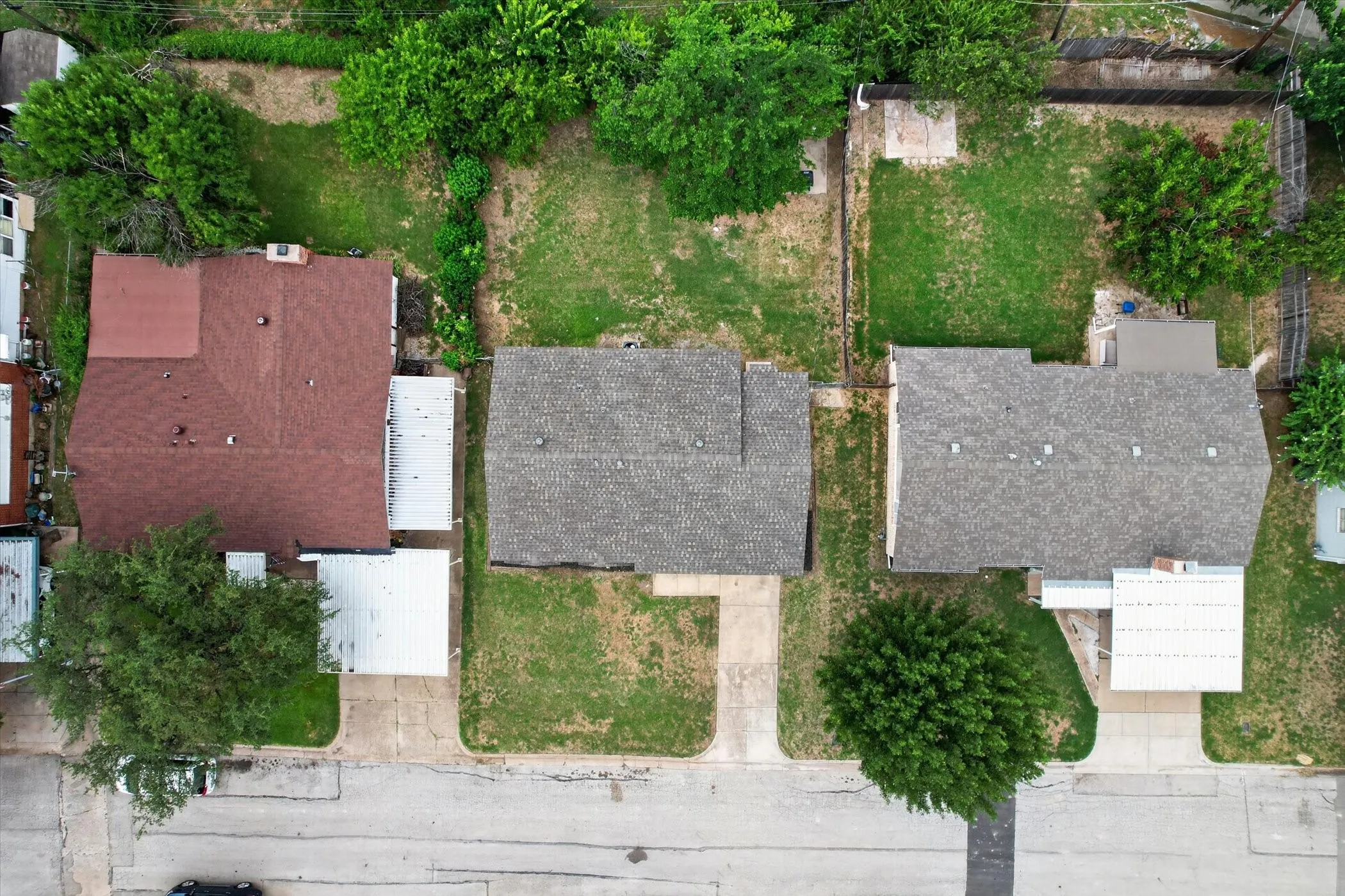 Aerial view showcasing three distinct properties, each with a pitched roof and a private driveway