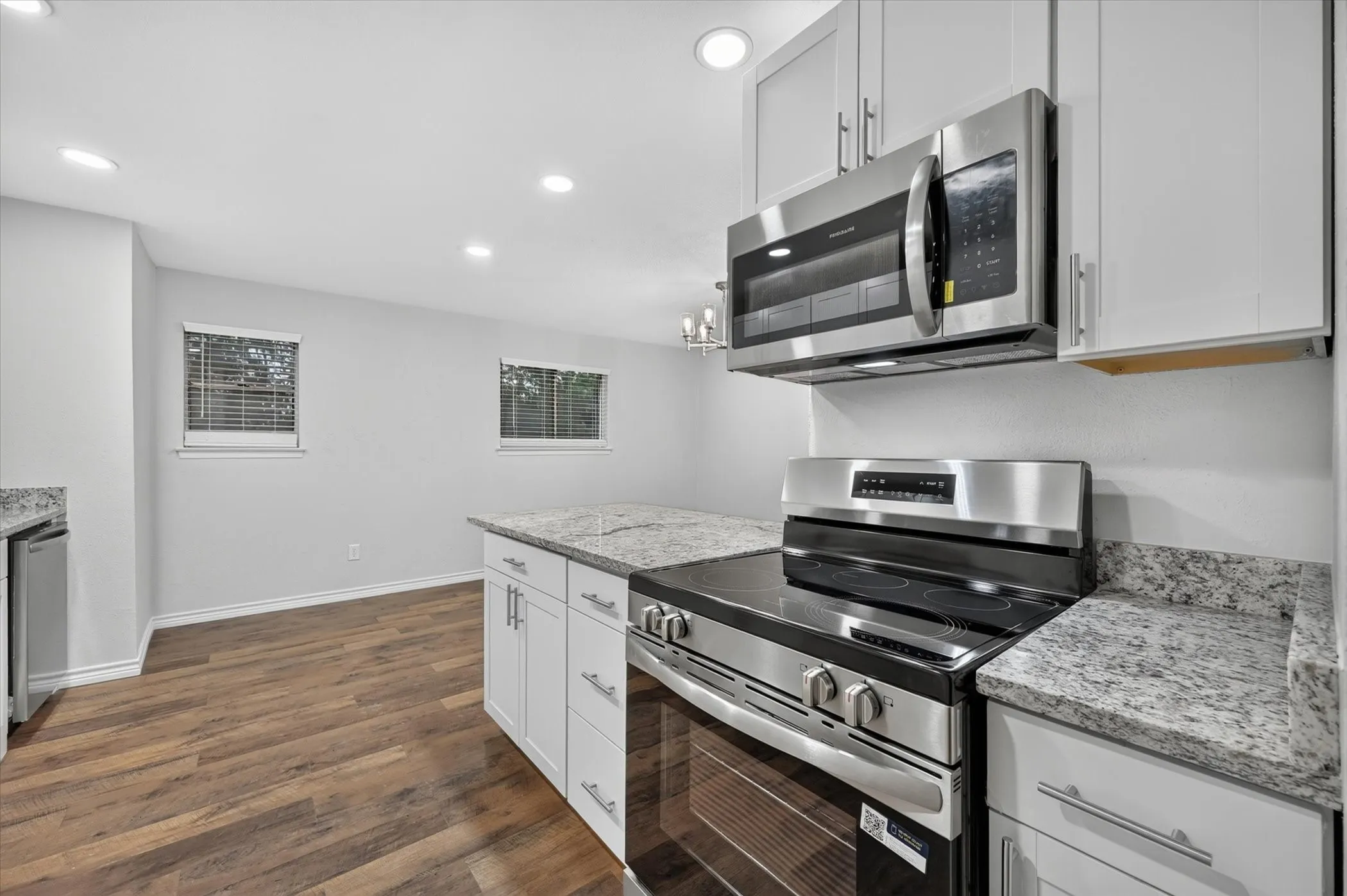 Kitchen featuring wood-finish flooring, recessed lighting, white cabinetry, granite countertops, and stainless steel appliances
