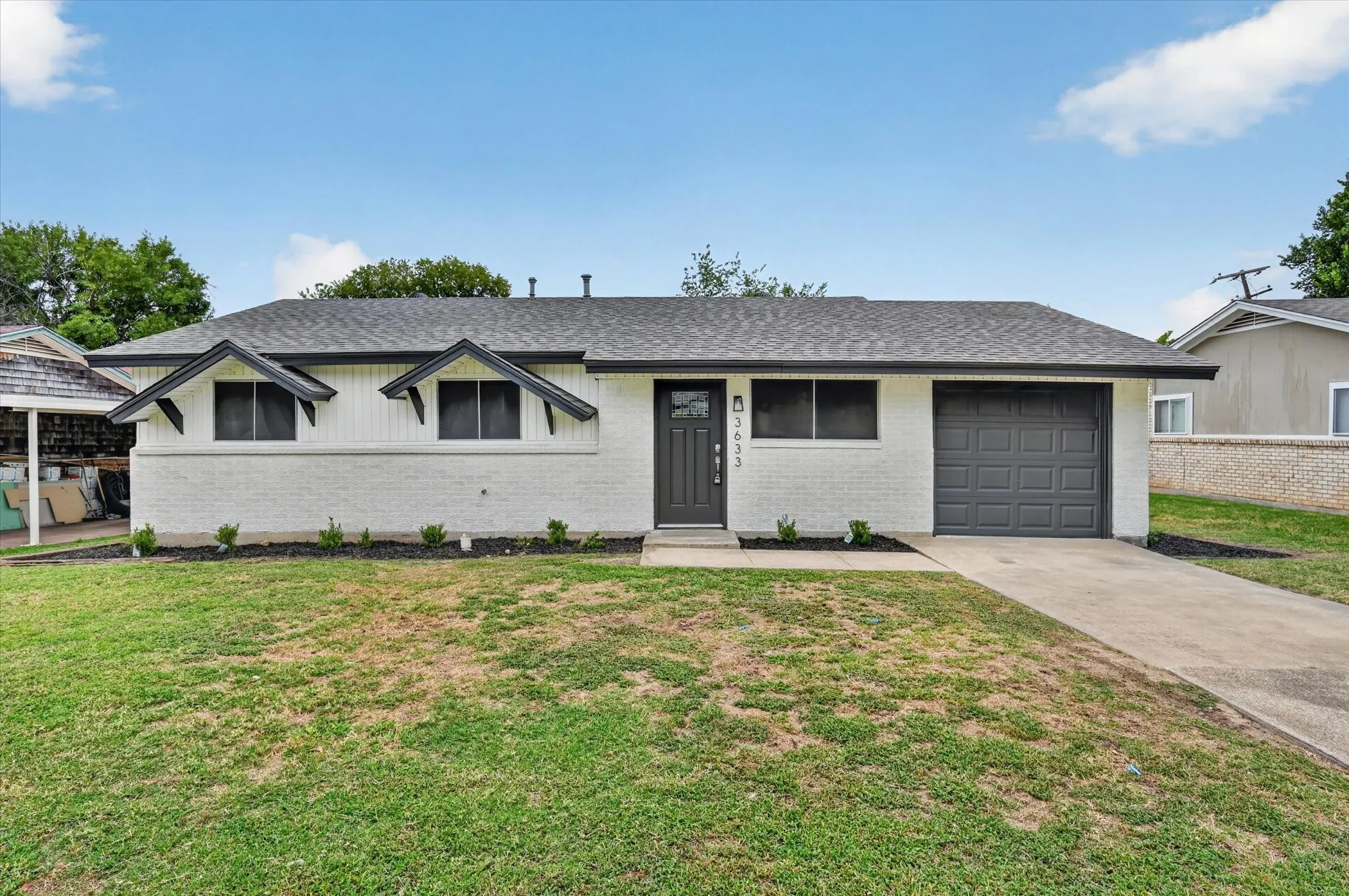 White brick exterior with dark trim accents and a gray shingle roof