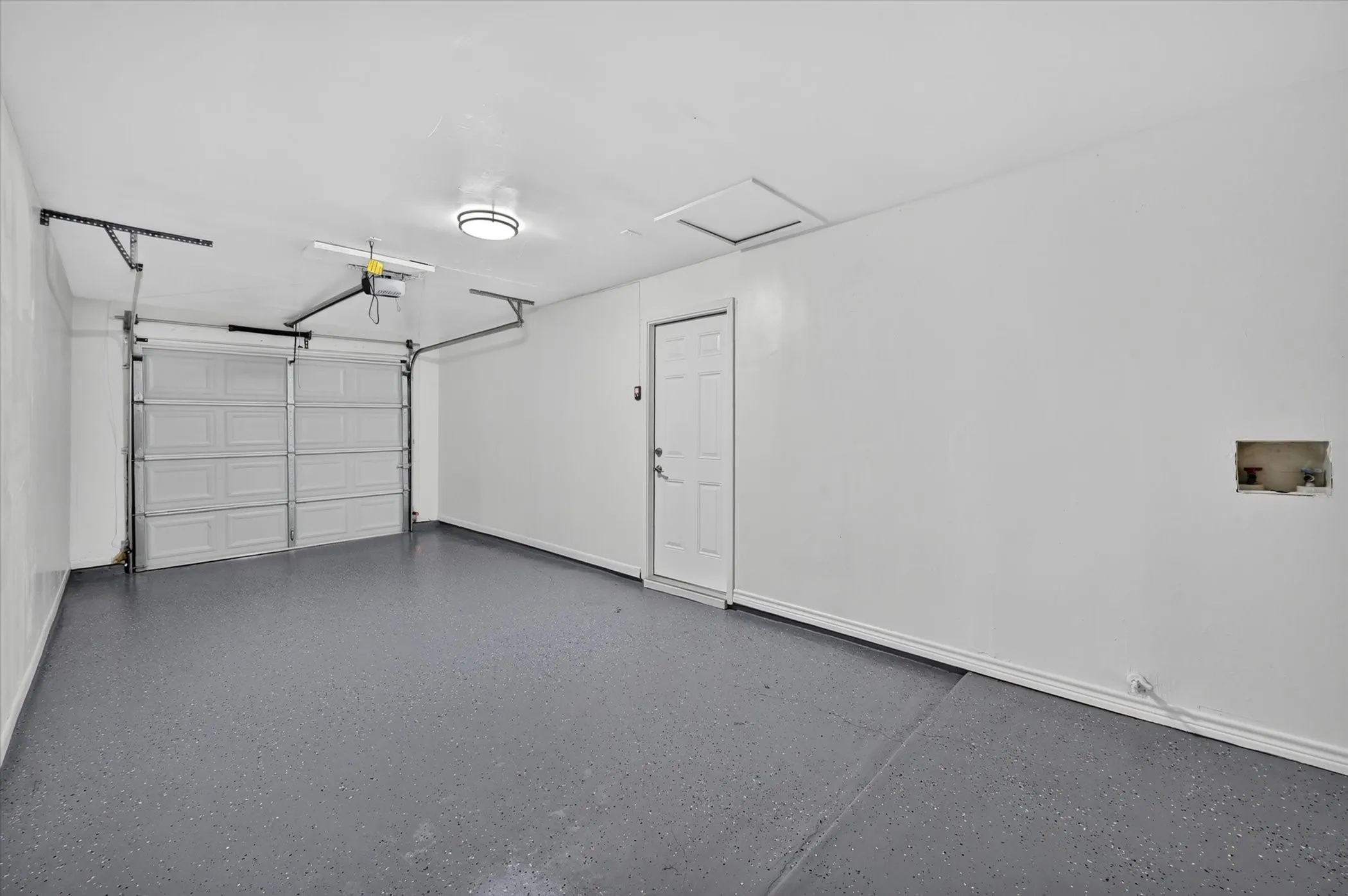 Spacious garage featuring a two-car overhead door, epoxy flooring, built-in overhead lighting, and interior access door