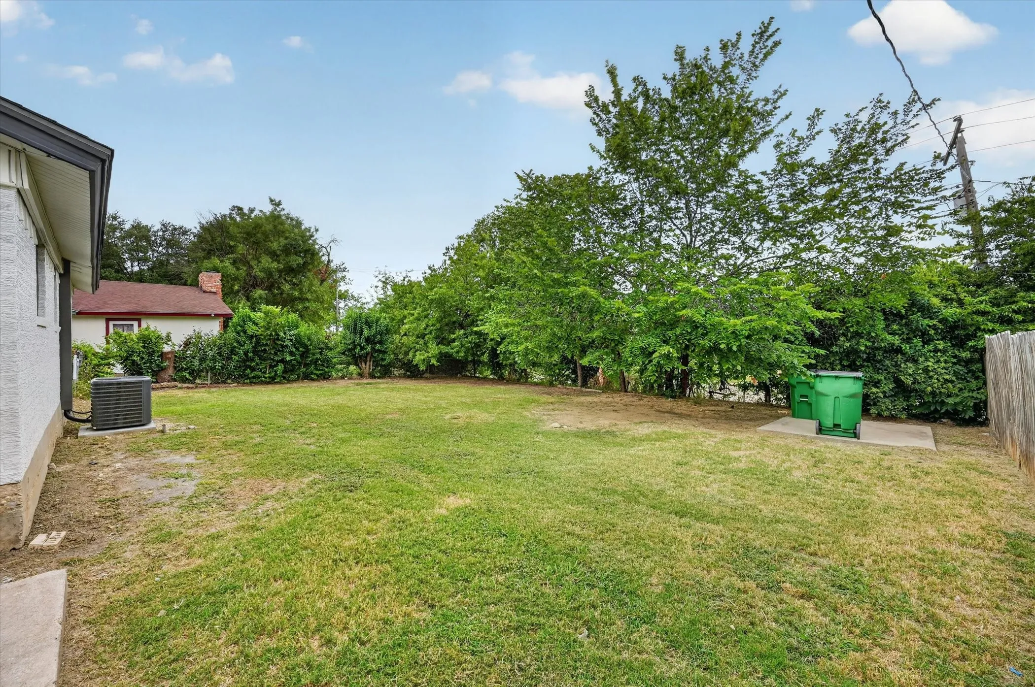 Expansive backyard with a manicured lawn, established trees, and a partial privacy fence