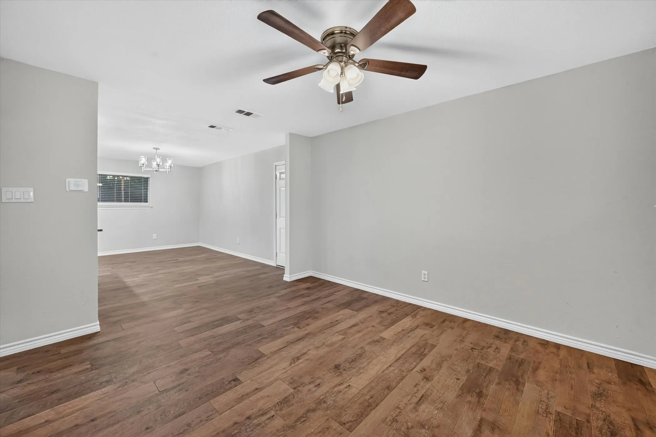 Spacious room featuring wood-finish flooring, light grey wall paint, and white baseboards