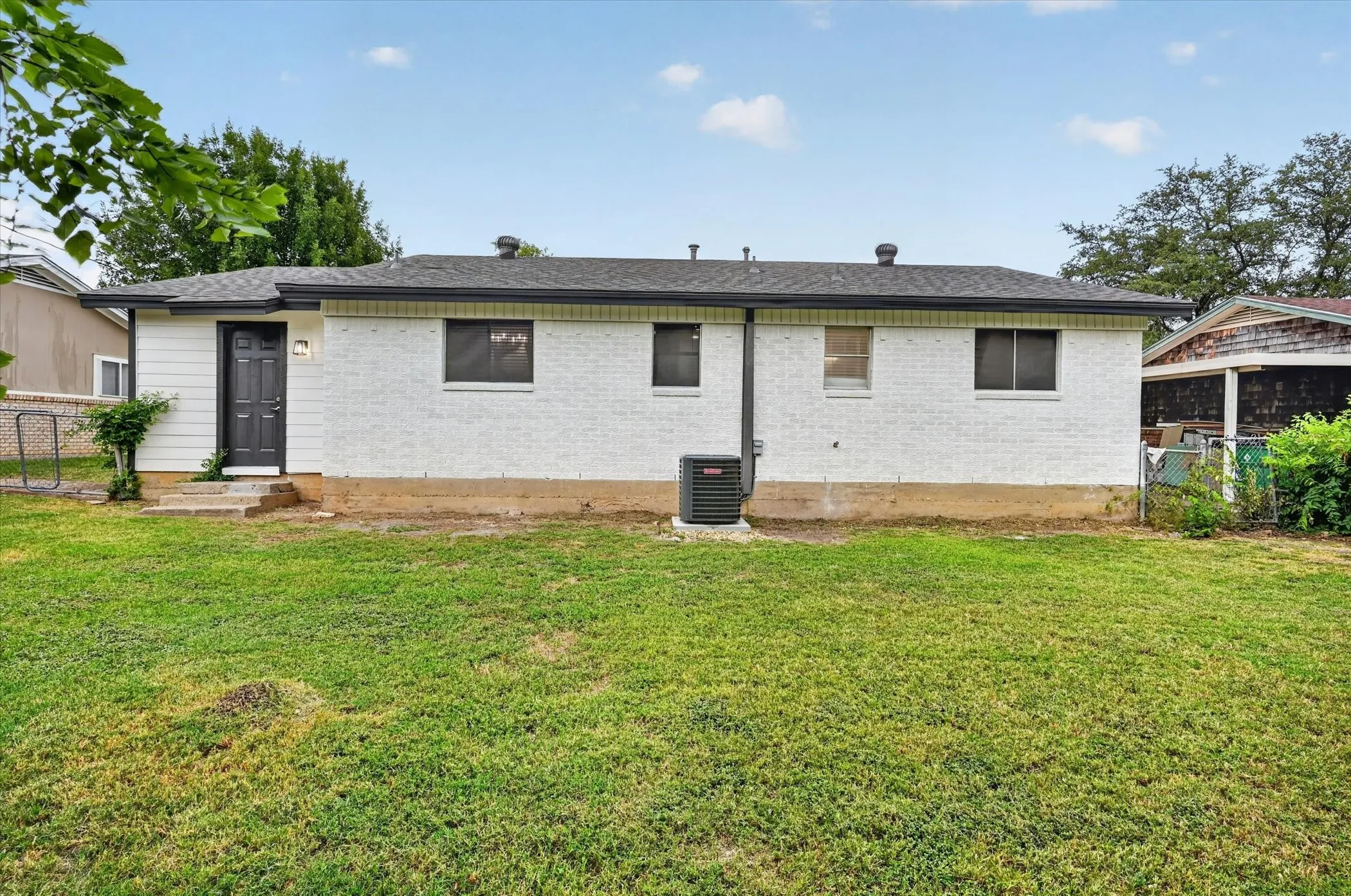 Rear exterior with white painted brick and siding, dark roof, dark rear entry door, and a grass lawn