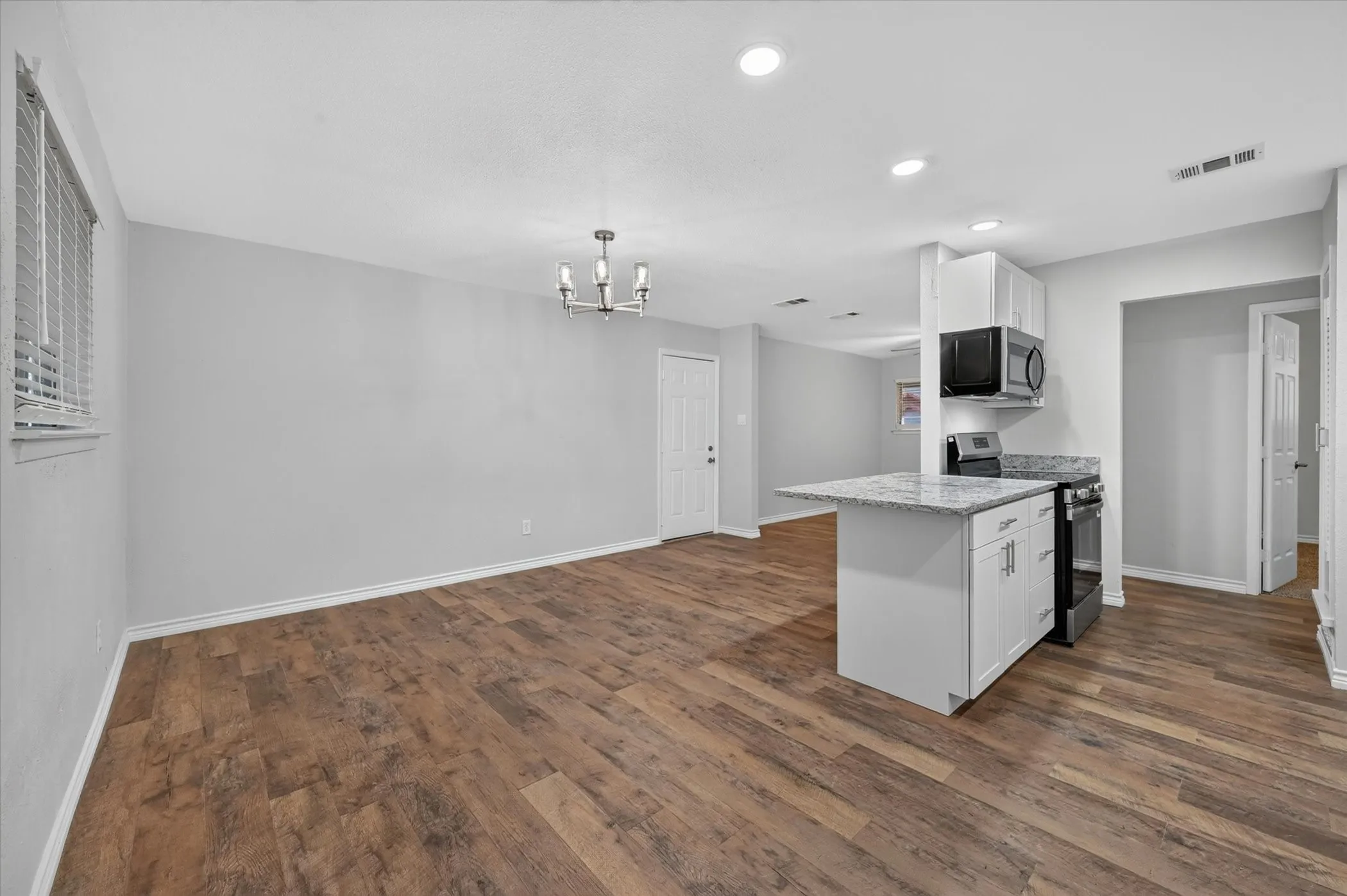 Open-concept living space with wood-finish flooring, recessed lighting, and a modern chandelier