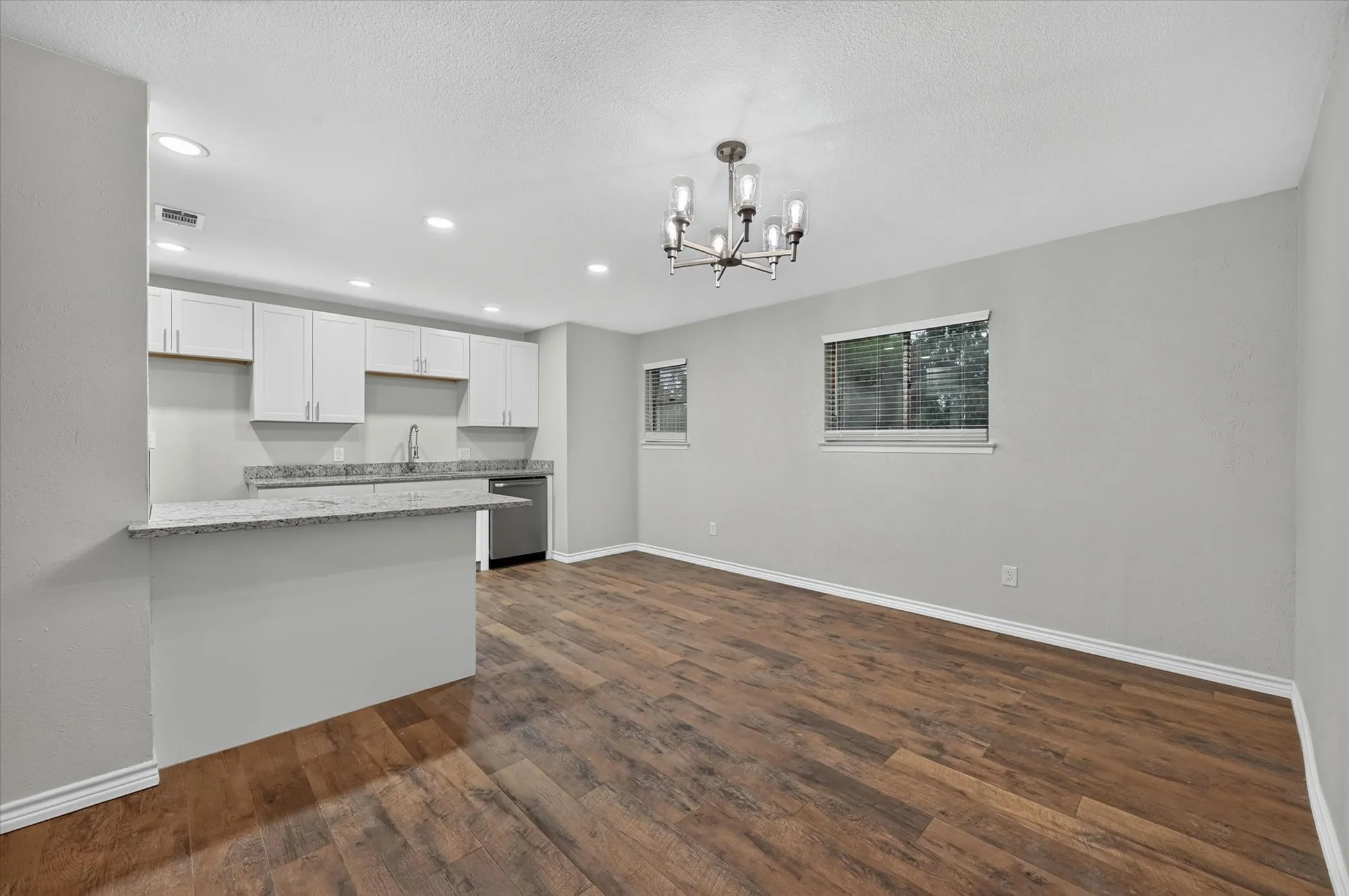 Open-concept living area featuring wood-finish flooring, a modern chandelier, and recessed lighting