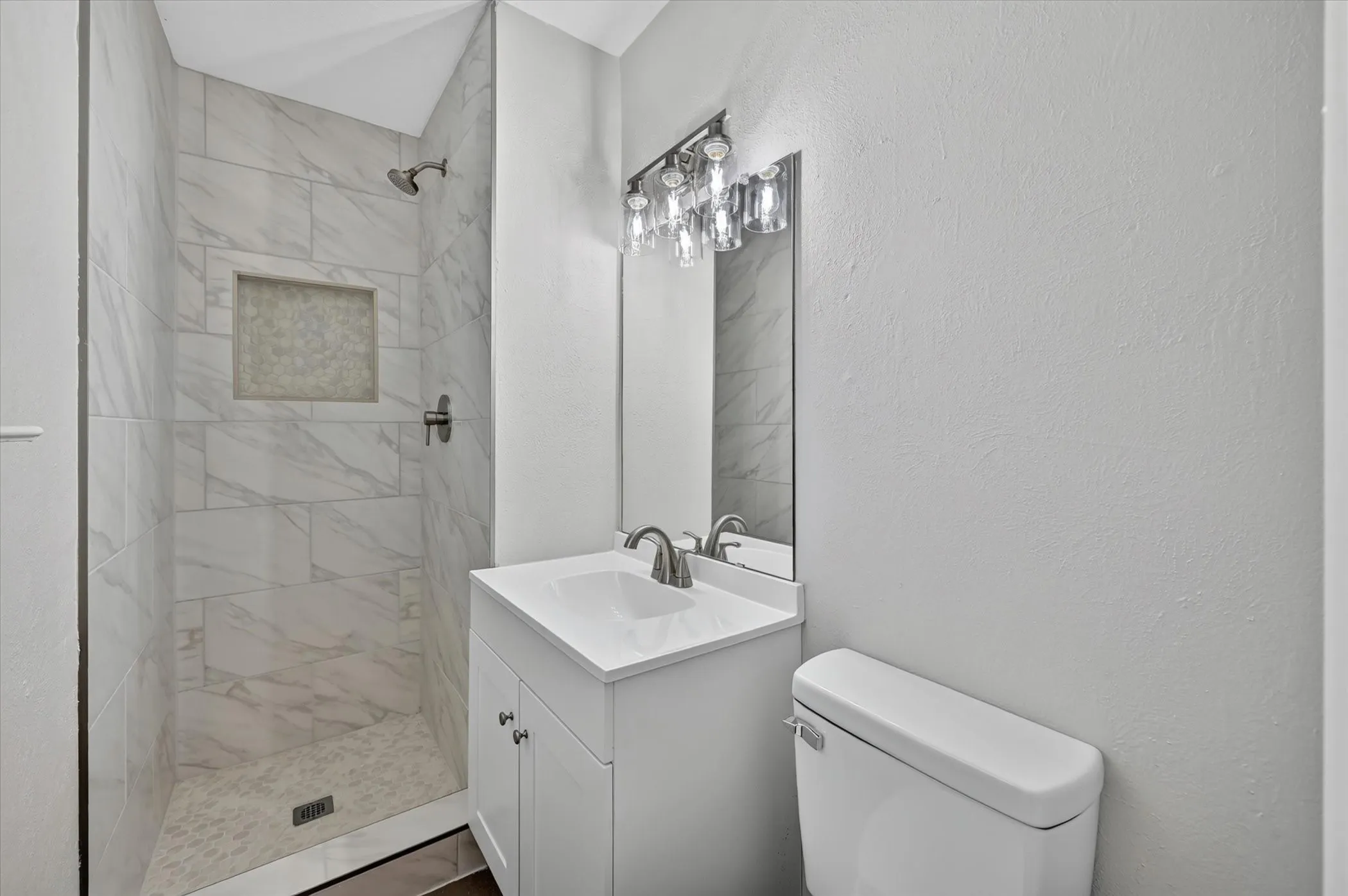 Bathroom featuring a tiled shower with a recessed niche, a single vanity with an integrated sink, and a modern light fixture