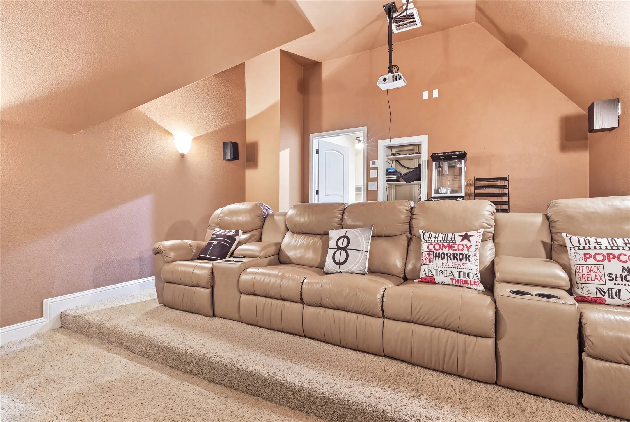 Dedicated media room featuring tiered carpeted flooring, built-in wall sconces, and sloped ceilings