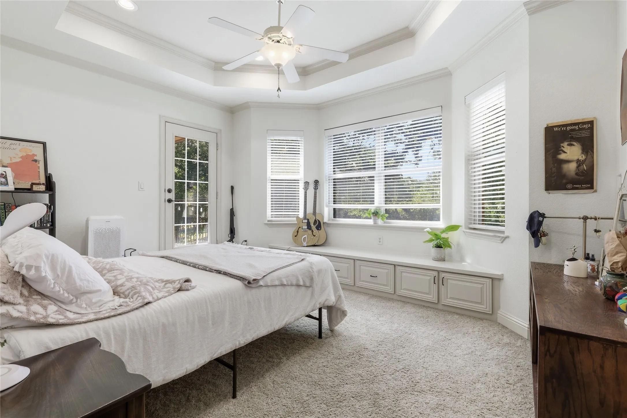 Carpeted room featuring a tray ceiling, ceiling fan, and a French door with glass panes, bedroom also has a door leading to outdoor balcony