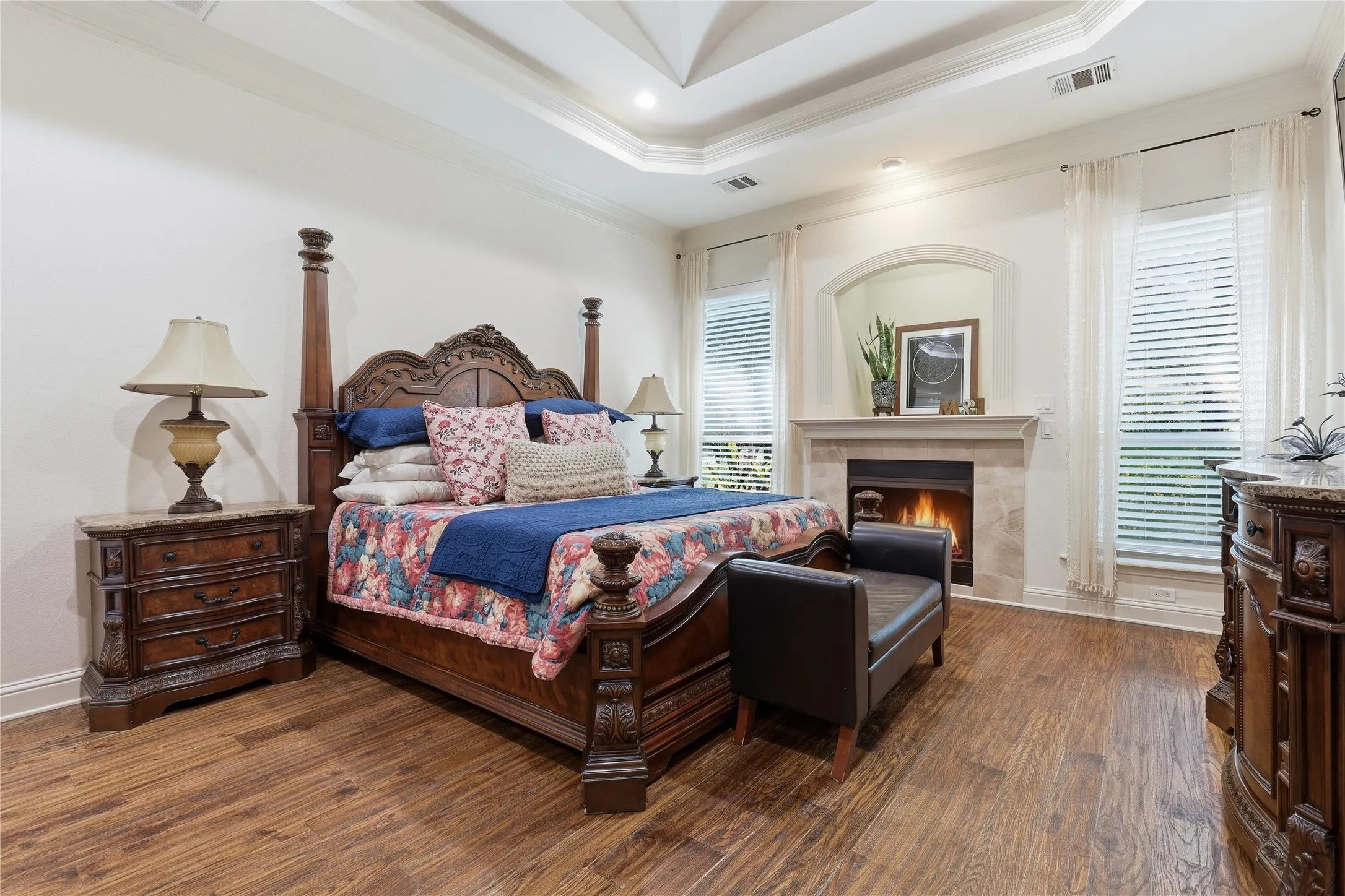 Spacious interior featuring wood-finish flooring, an arched fireplace with a light-toned mantel, dual windows with blinds, a tray ceiling, and recessed lighting
