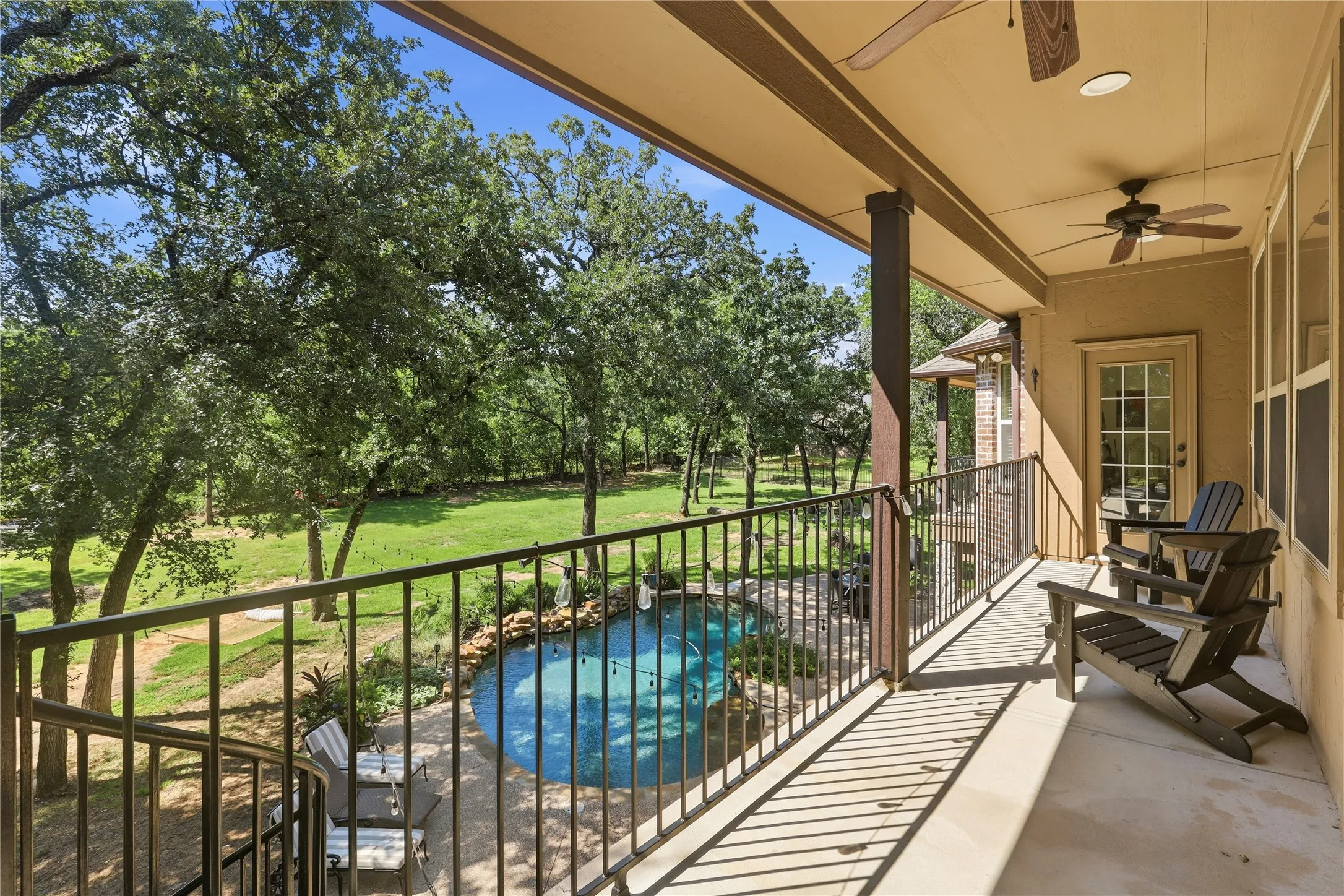 Upper-level covered balcony featuring a light-toned concrete surface, black metal railing, and a pair of ceiling fans