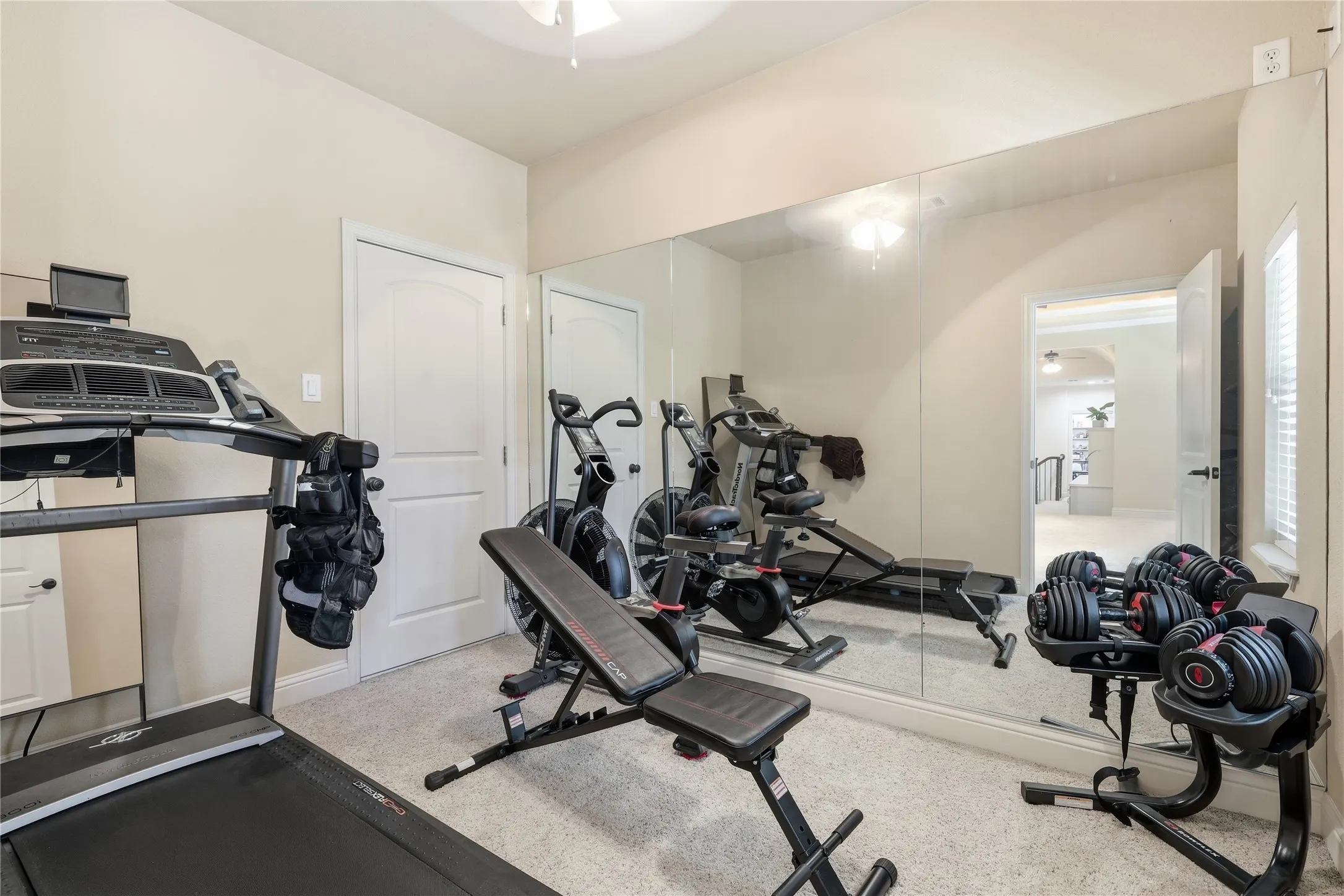 Flex space featuring wall-to-wall mirrors, light-colored carpeting, a white paneled door, and a ceiling fan