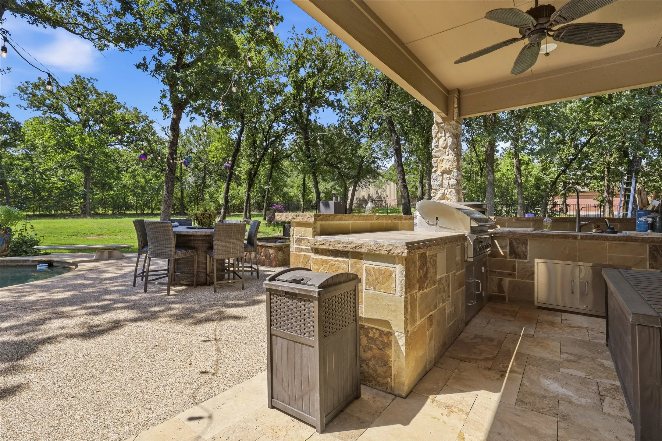 Expansive outdoor kitchen and dining area featuring a built-in grill, stone-clad counters, and a ceiling fan