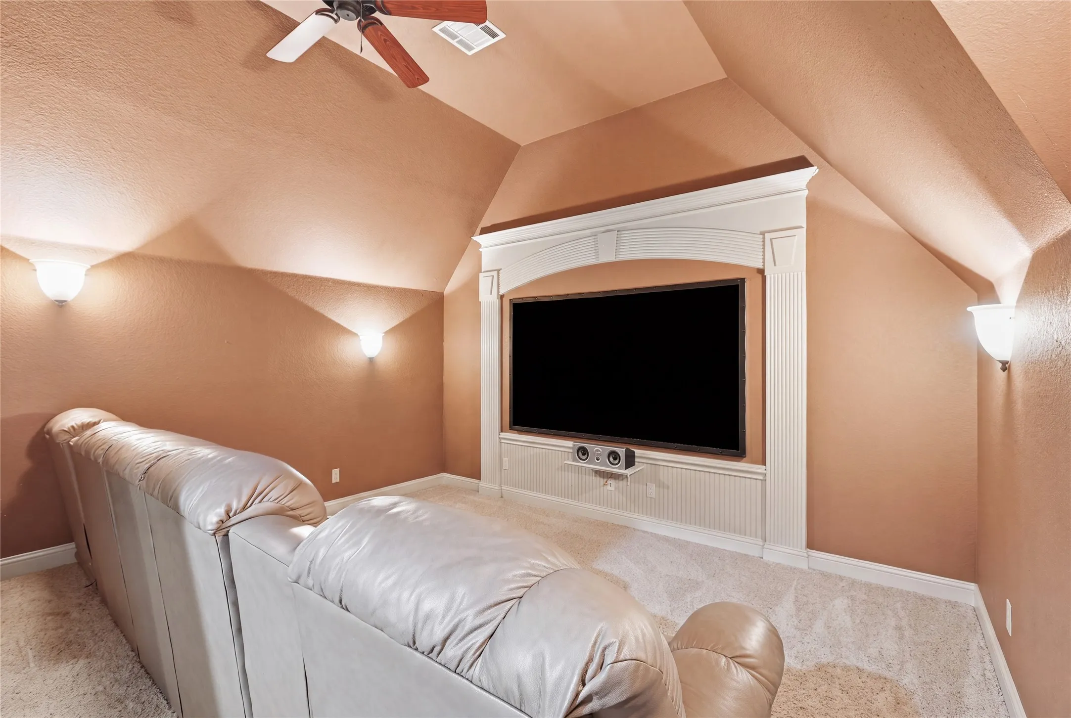 Built-in media center with decorative molding, wall-mounted sconce lighting, angled ceiling, ceiling fan, and carpet flooring