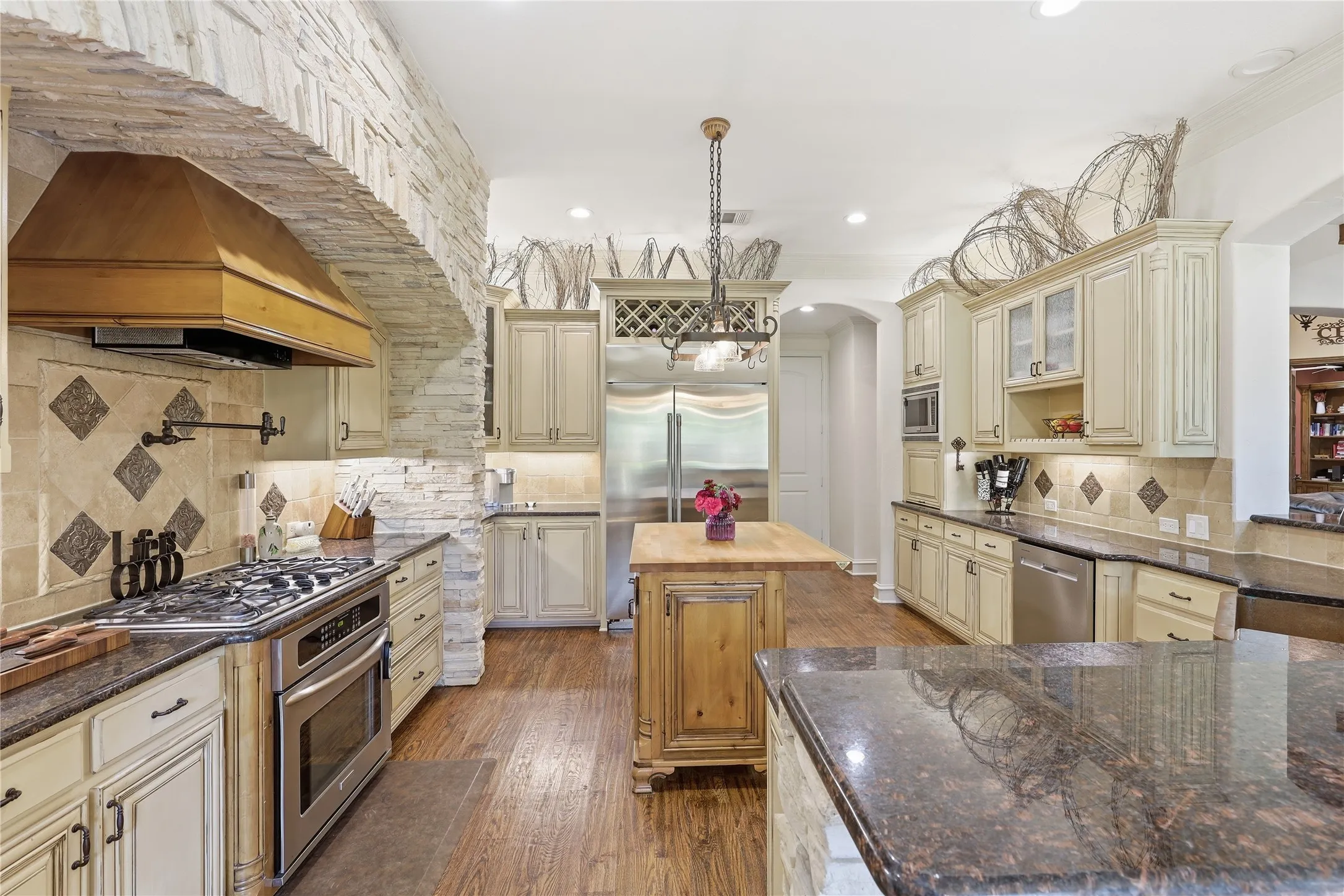 Spacious kitchen featuring stone accent walls, wood-finish flooring, custom cabinetry, granite countertops, and stainless steel appliances