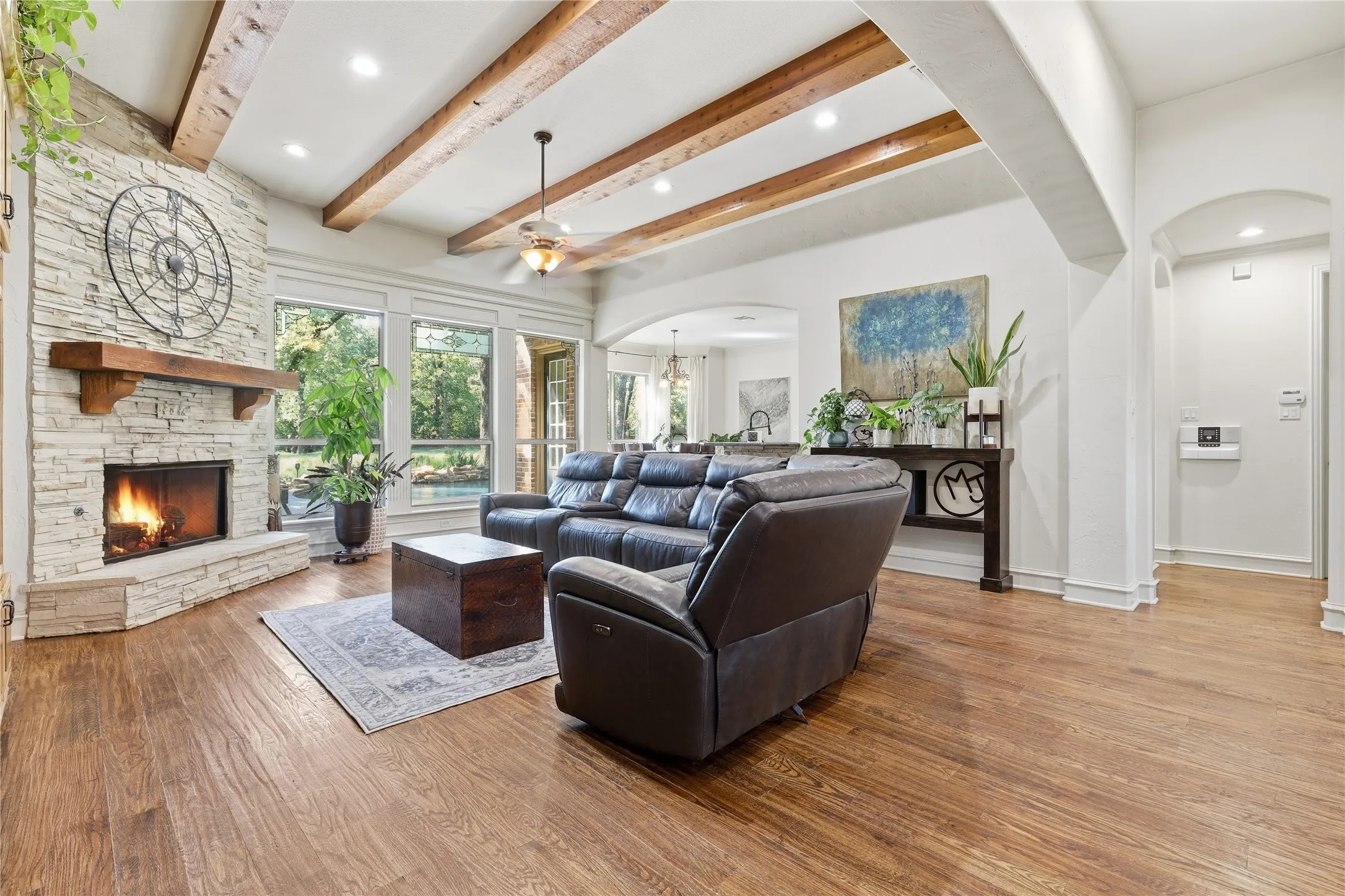Spacious living area featuring a stone-clad fireplace with a wood mantel, exposed wood ceiling beams, and wood-finish flooring