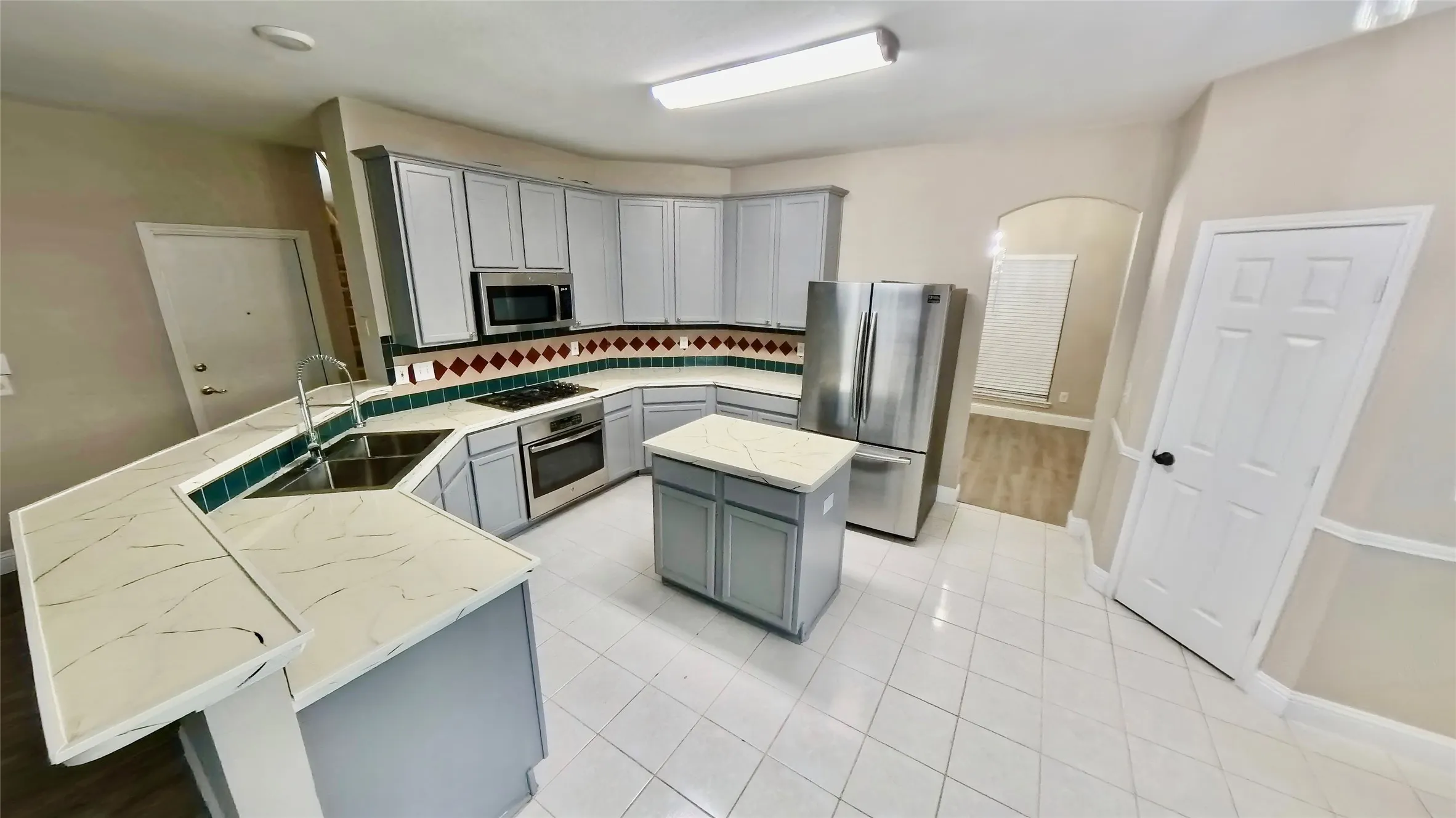 Kitchen featuring gray cabinetry, light stone countertops, sink, stainless steel appliances, and a kitchen island