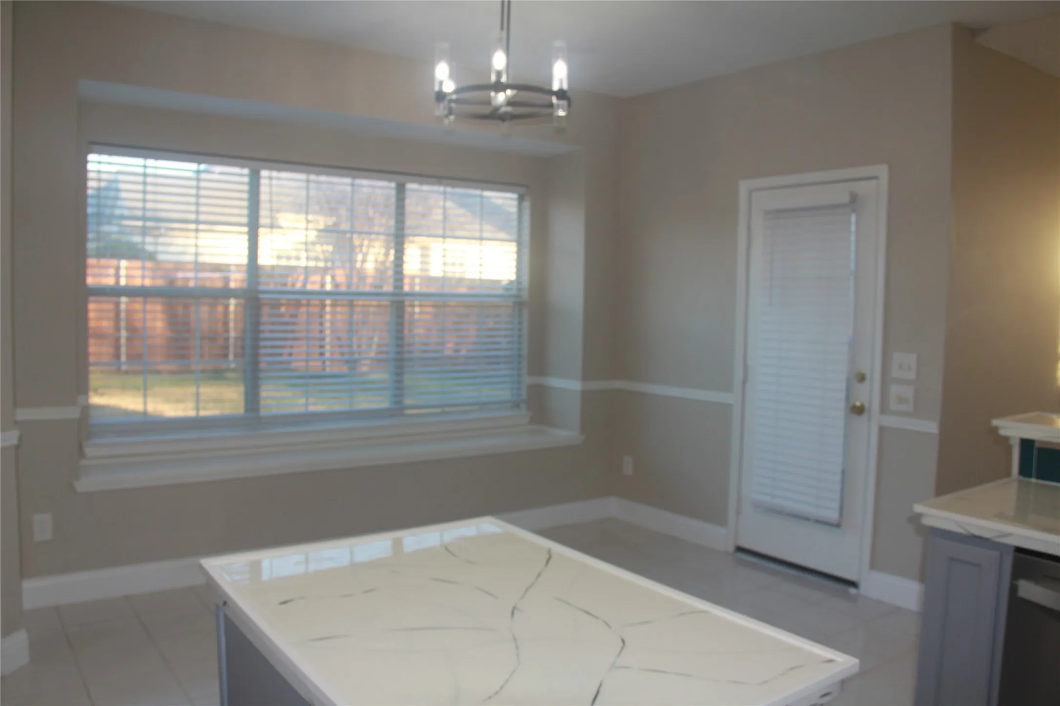Kitchen featuring light stone countertops, hanging light fixtures, an inviting chandelier, white dishwasher, and light tile patterned floors