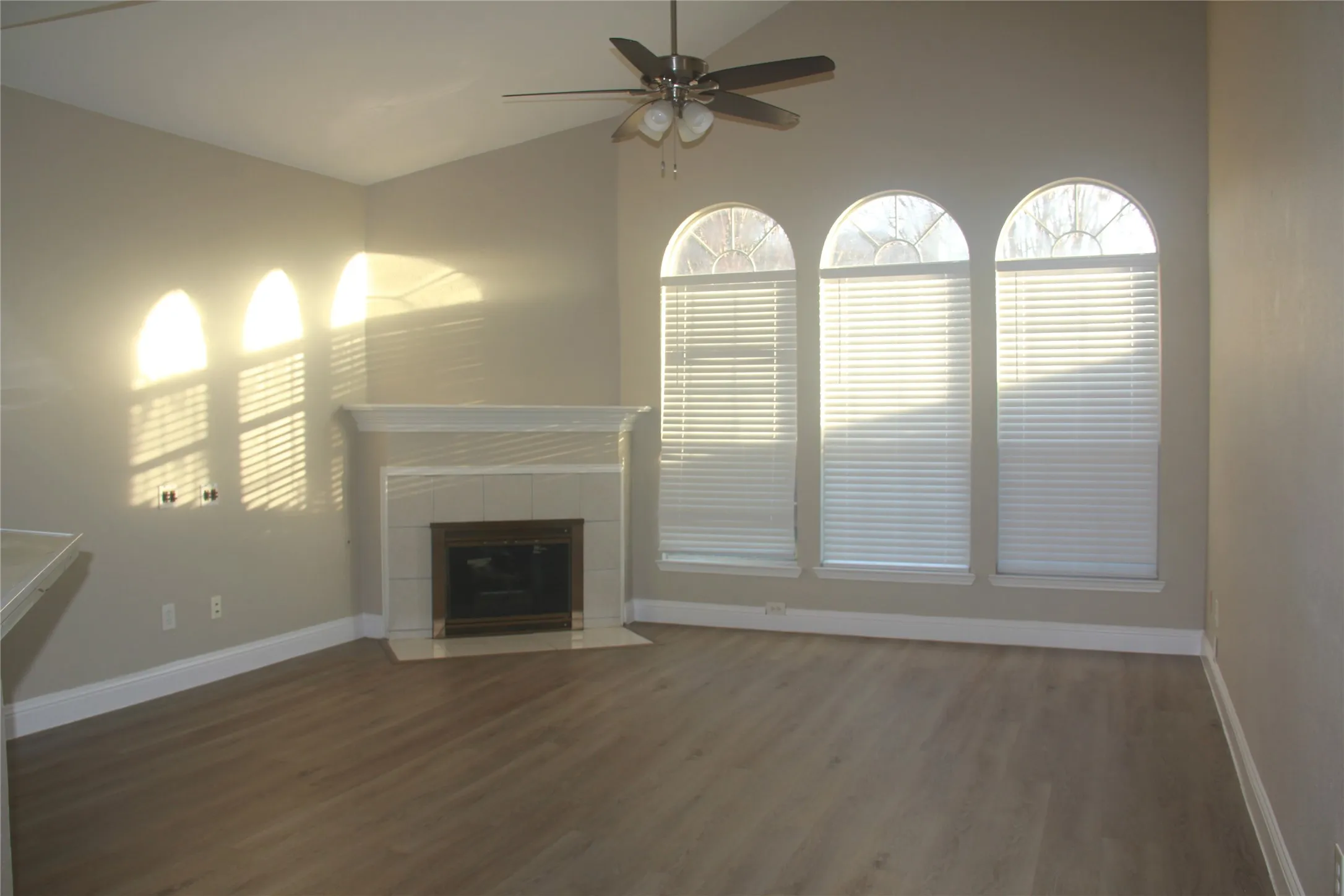 Unfurnished living room with ceiling fan, dark hardwood / wood-style flooring, a tile fireplace, and vaulted ceiling