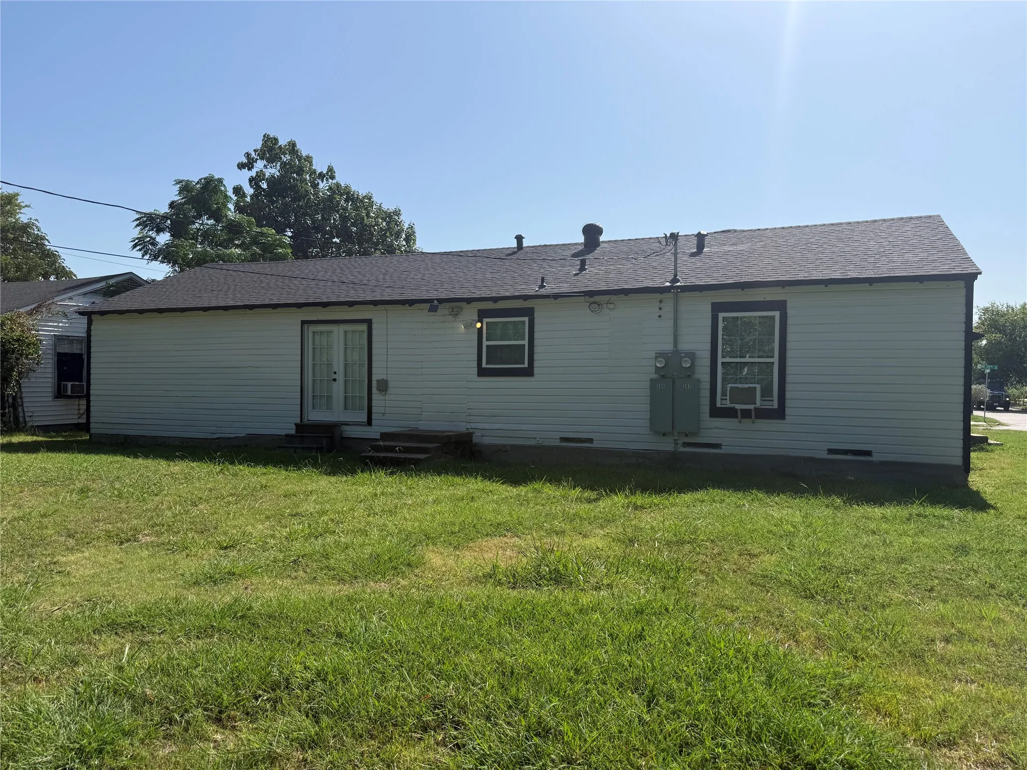 Rear exterior featuring light-colored siding, a dark asphalt shingle roof, and a grassy yard