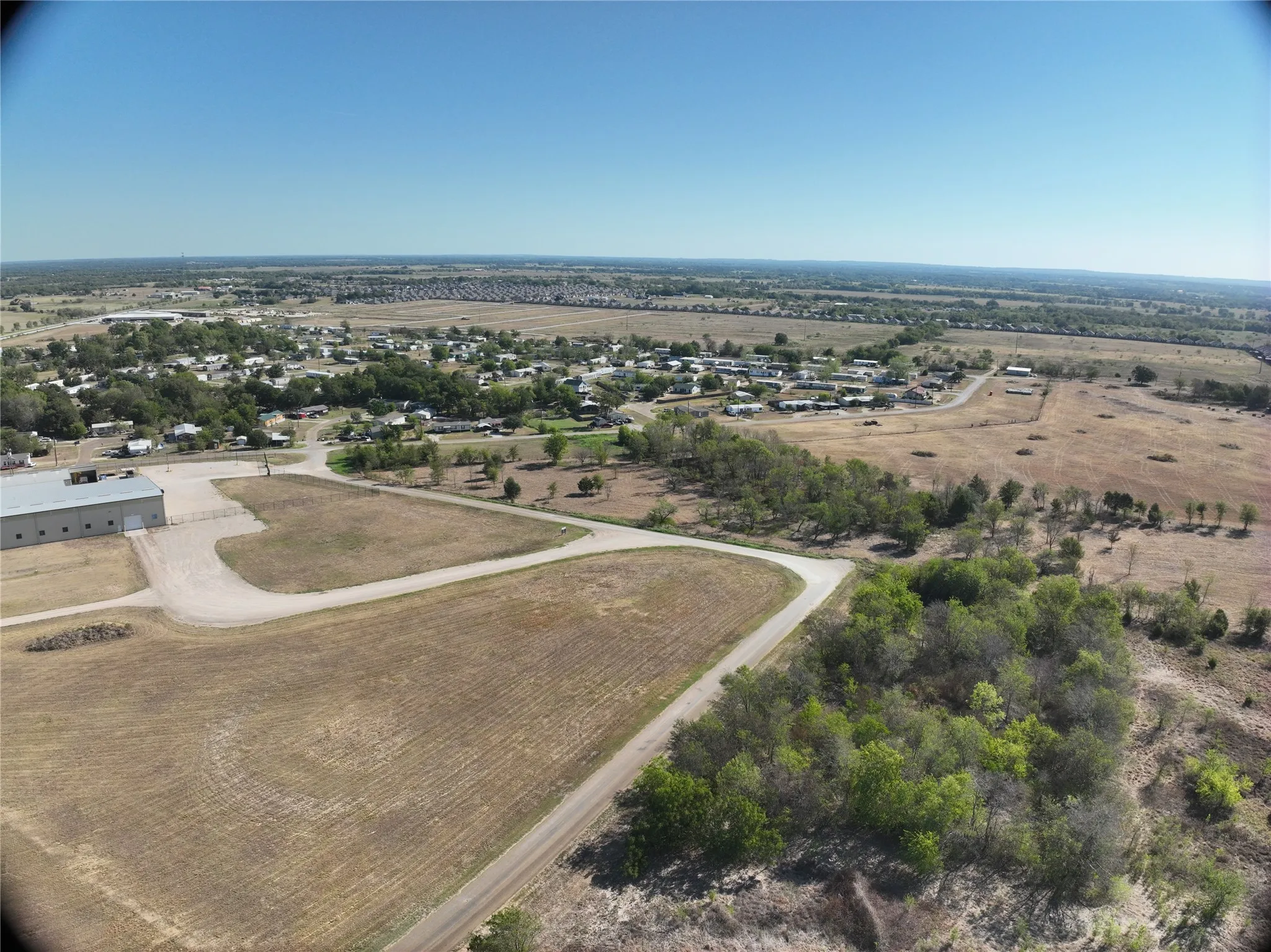 Expansive land parcel featuring clear skies, distant residential structures, and established roads