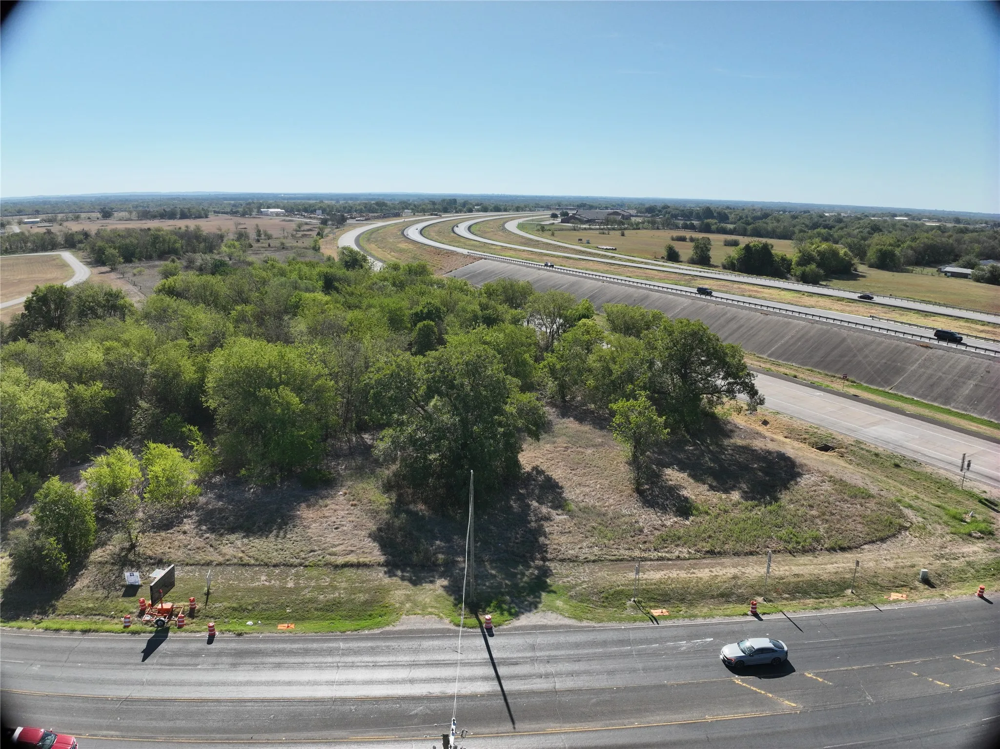 Expansive natural landscape with mature trees, adjacent to a multi-lane highway, featuring a clear sky overhead