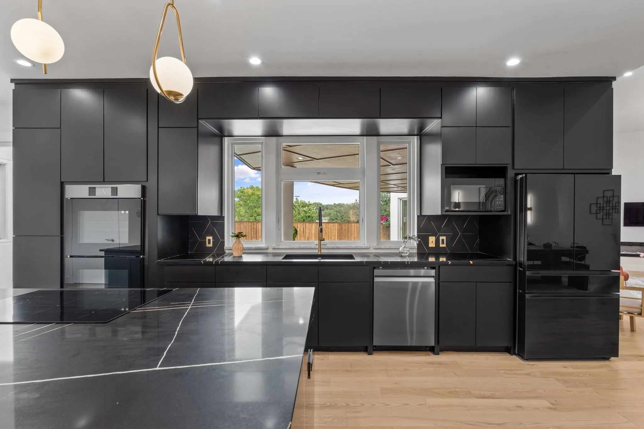Modern kitchen featuring dark cabinetry, a large kitchen island with a stone countertop, built-in stainless steel oven, integrated refrigerator, and light wood-finish flooring