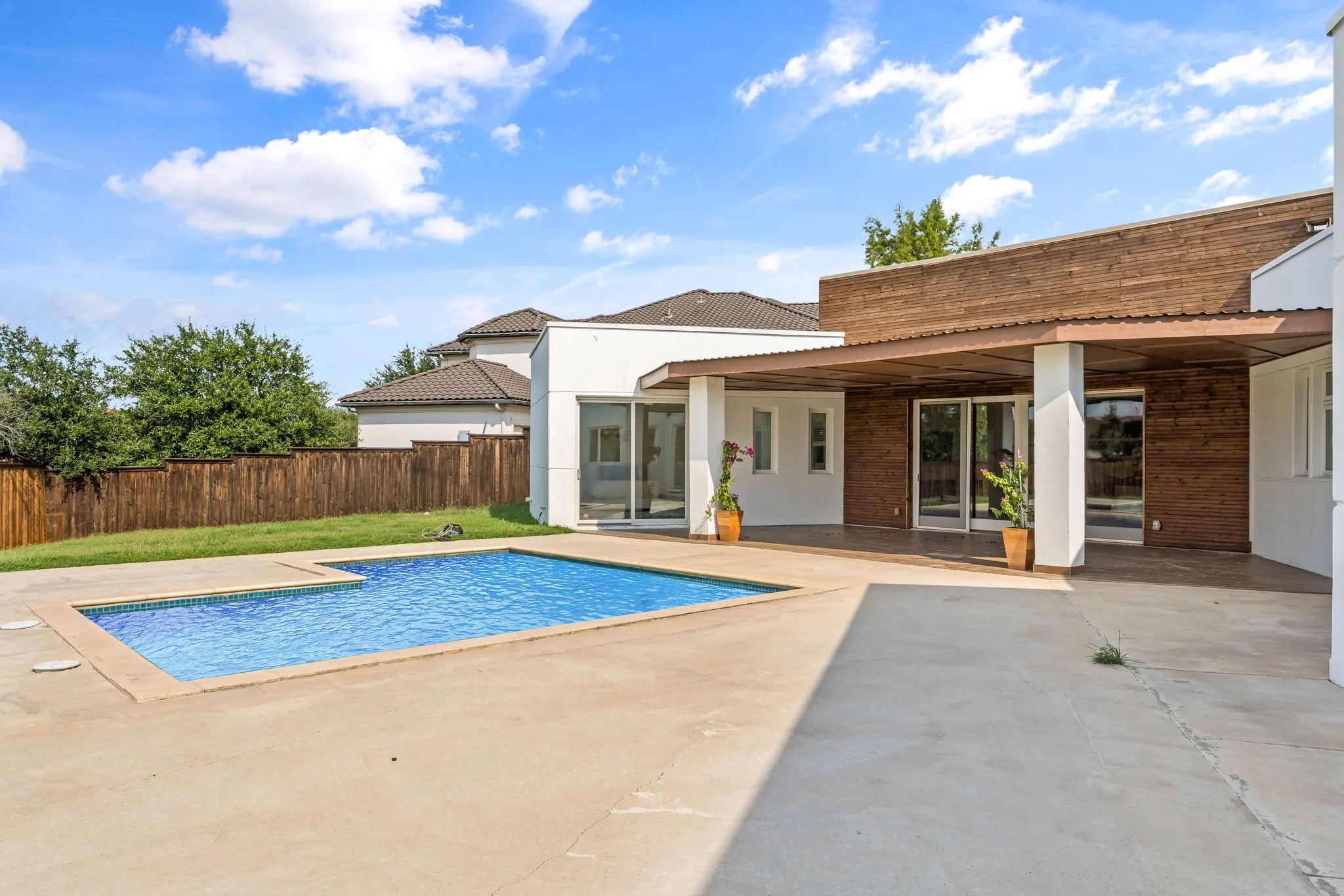 Rectangular swimming pool with integrated sun ledge, surrounded by expansive concrete decking