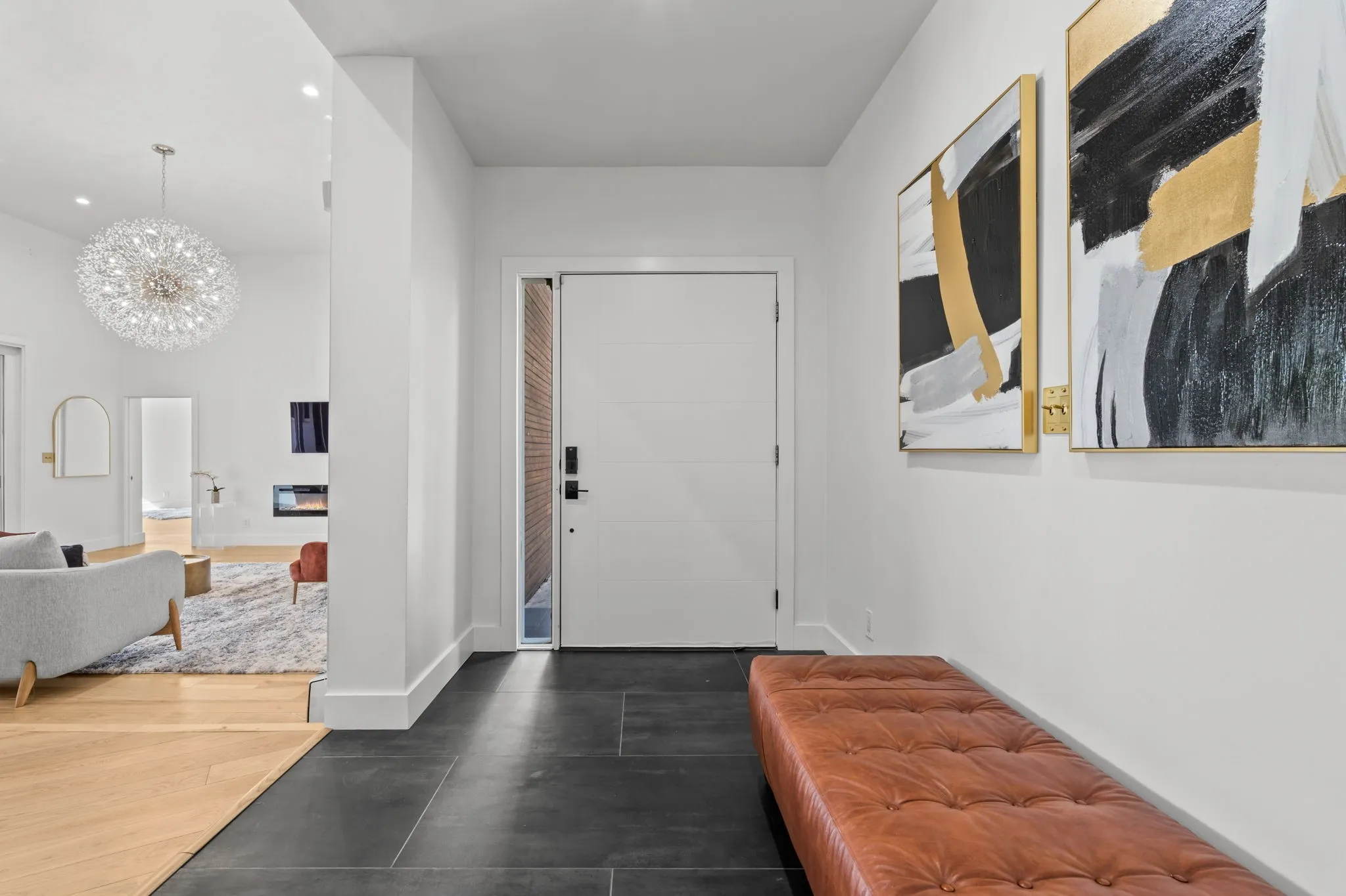 Entryway featuring dark tile flooring, a modern white door with a vertical window, and an adjacent living area with wood-finish flooring and a spherical chandelier