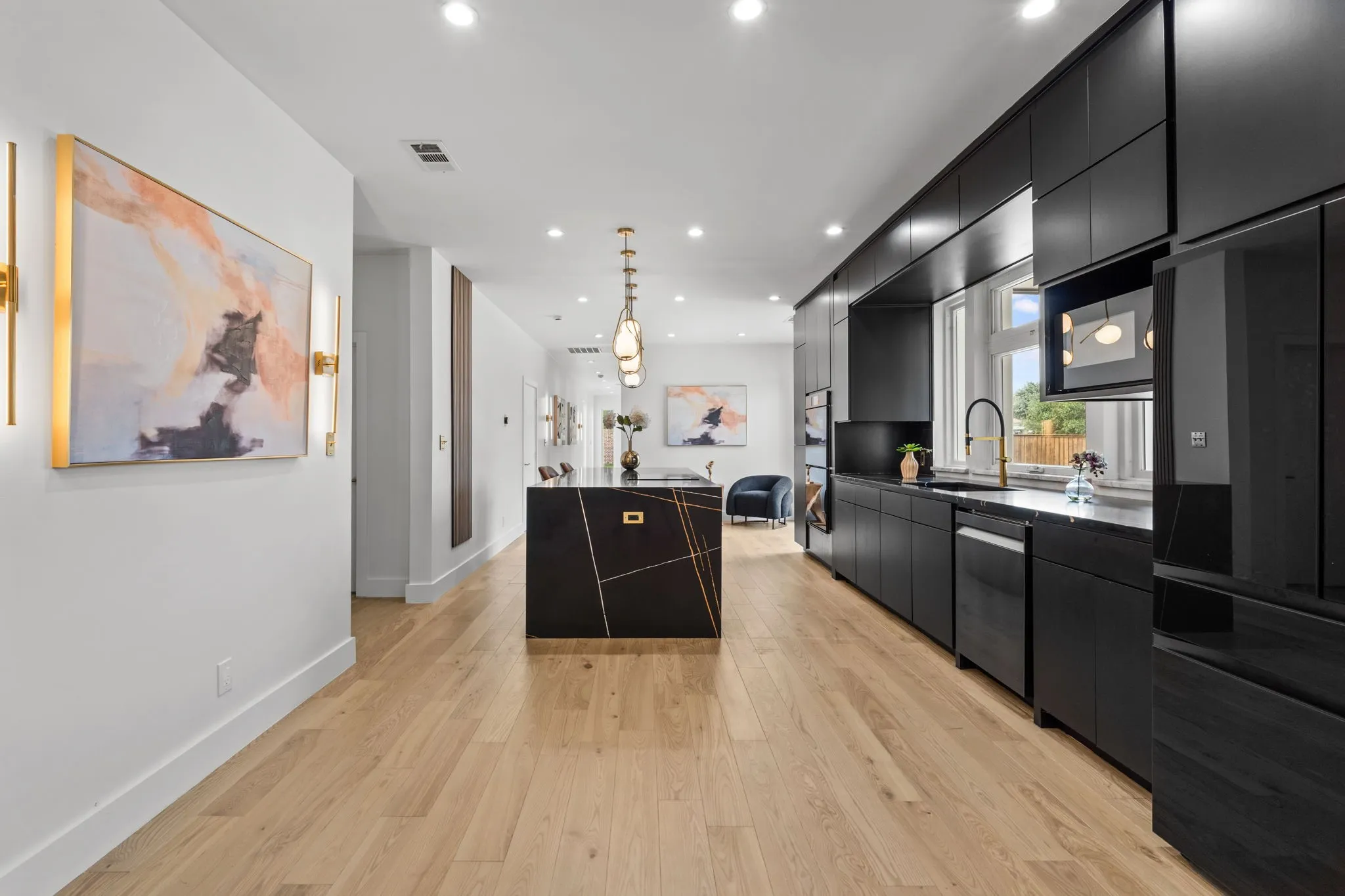 Modern kitchen featuring sleek black cabinetry, a waterfall island with gold-toned accents, and light wood-finish flooring