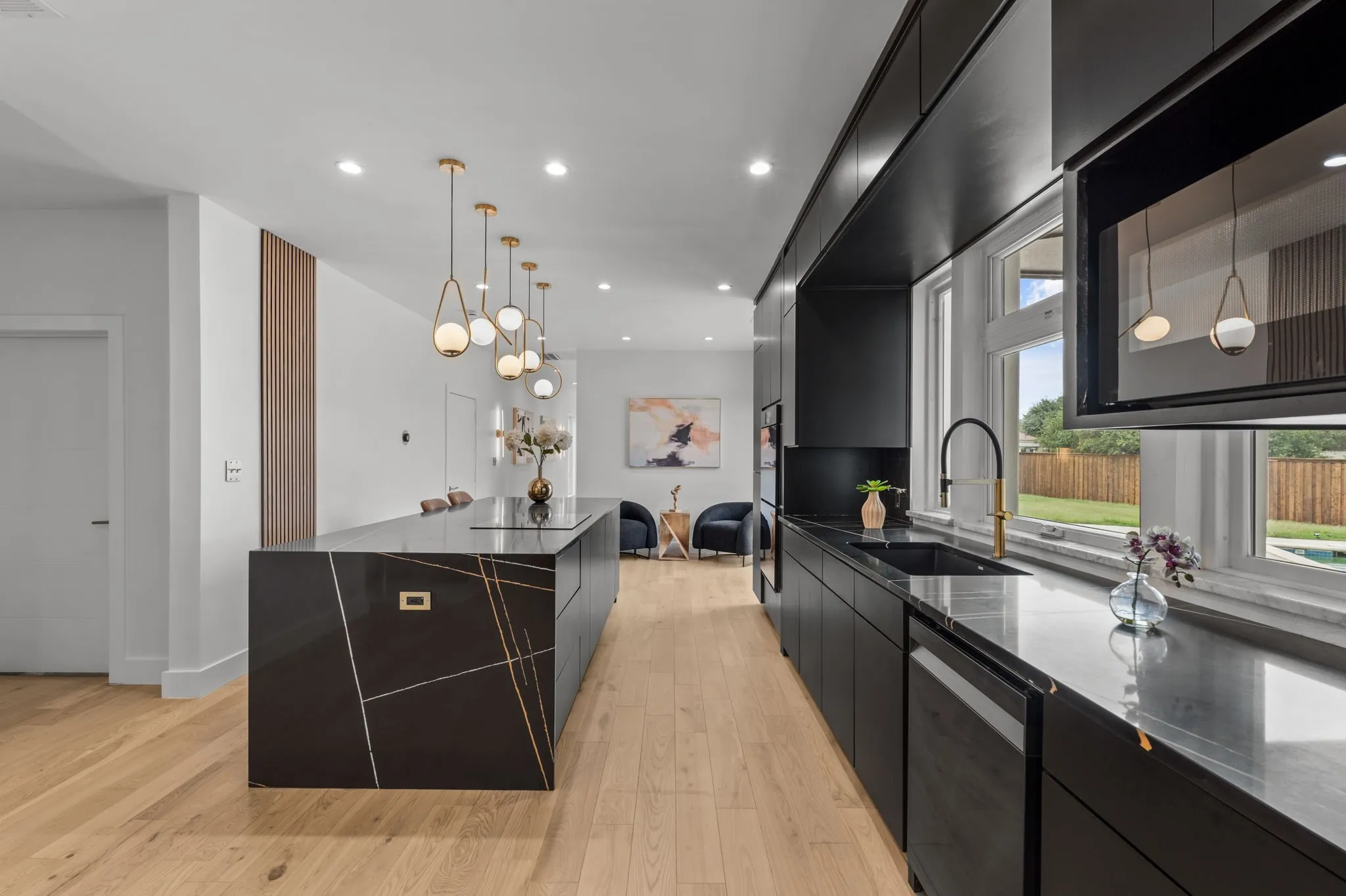 Modern kitchen featuring a large island with integrated cooktop, black cabinetry, and wood-finish flooring