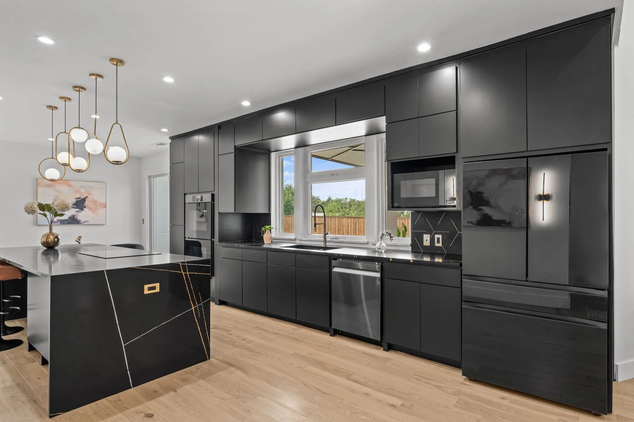 Contemporary kitchen featuring black cabinetry, light wood-finish flooring, recessed lighting, and a black and gold accent island
