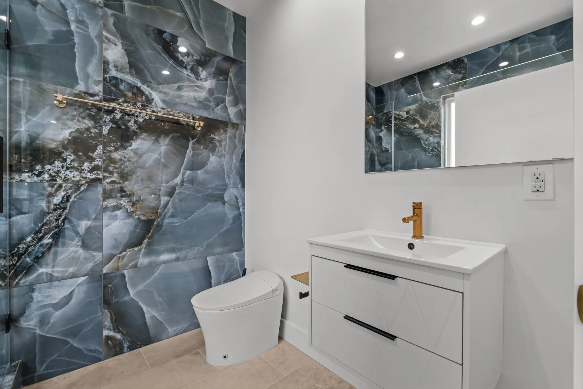 Bathroom featuring a stone-look accent wall, a wall-mounted vanity with a white countertop basin, and a gold-finish faucet