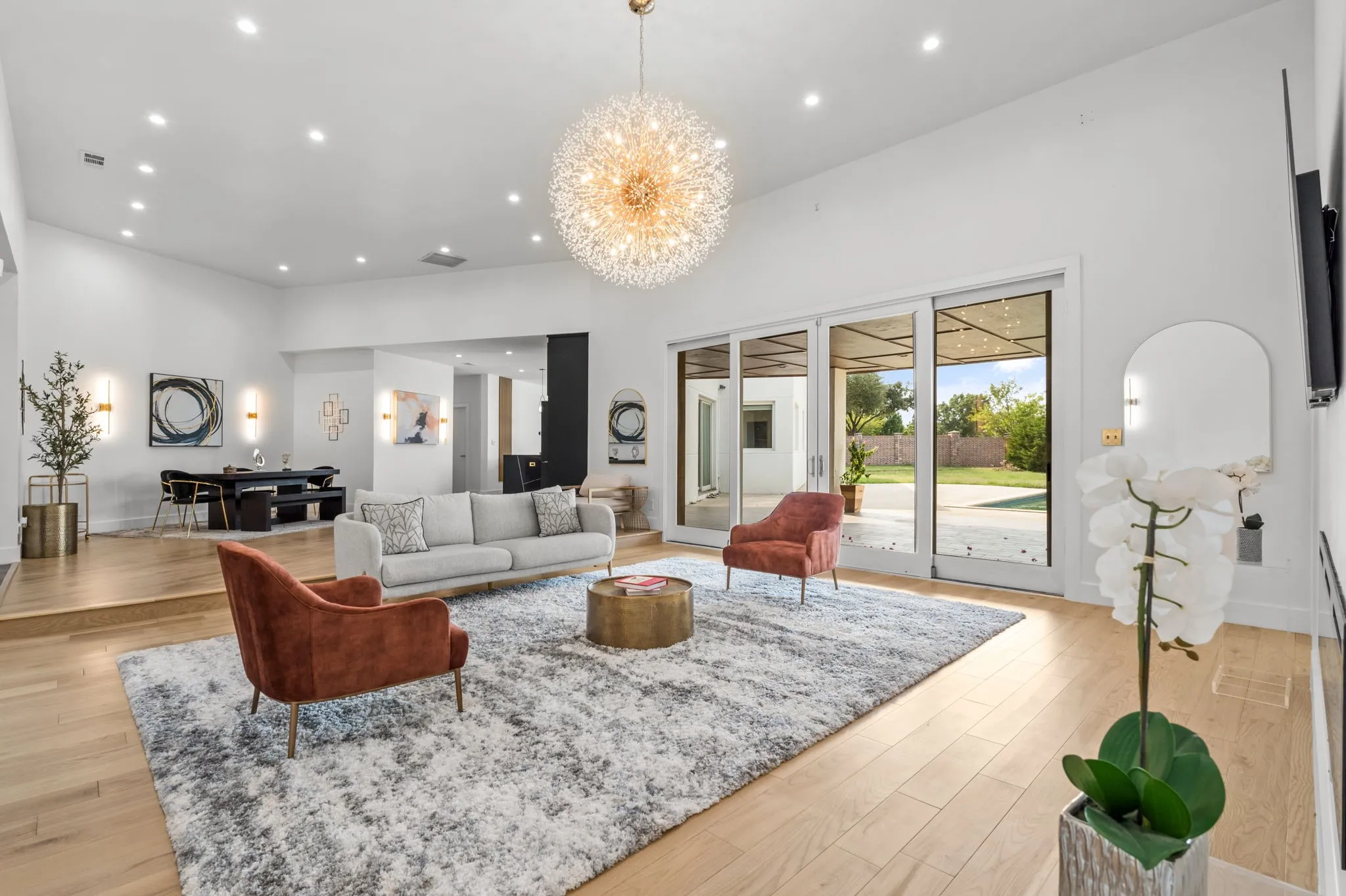 Spacious living area featuring light wood-finish flooring, a contemporary chandelier, recessed lighting, and large sliding glass doors opening to an outdoor patio and yard