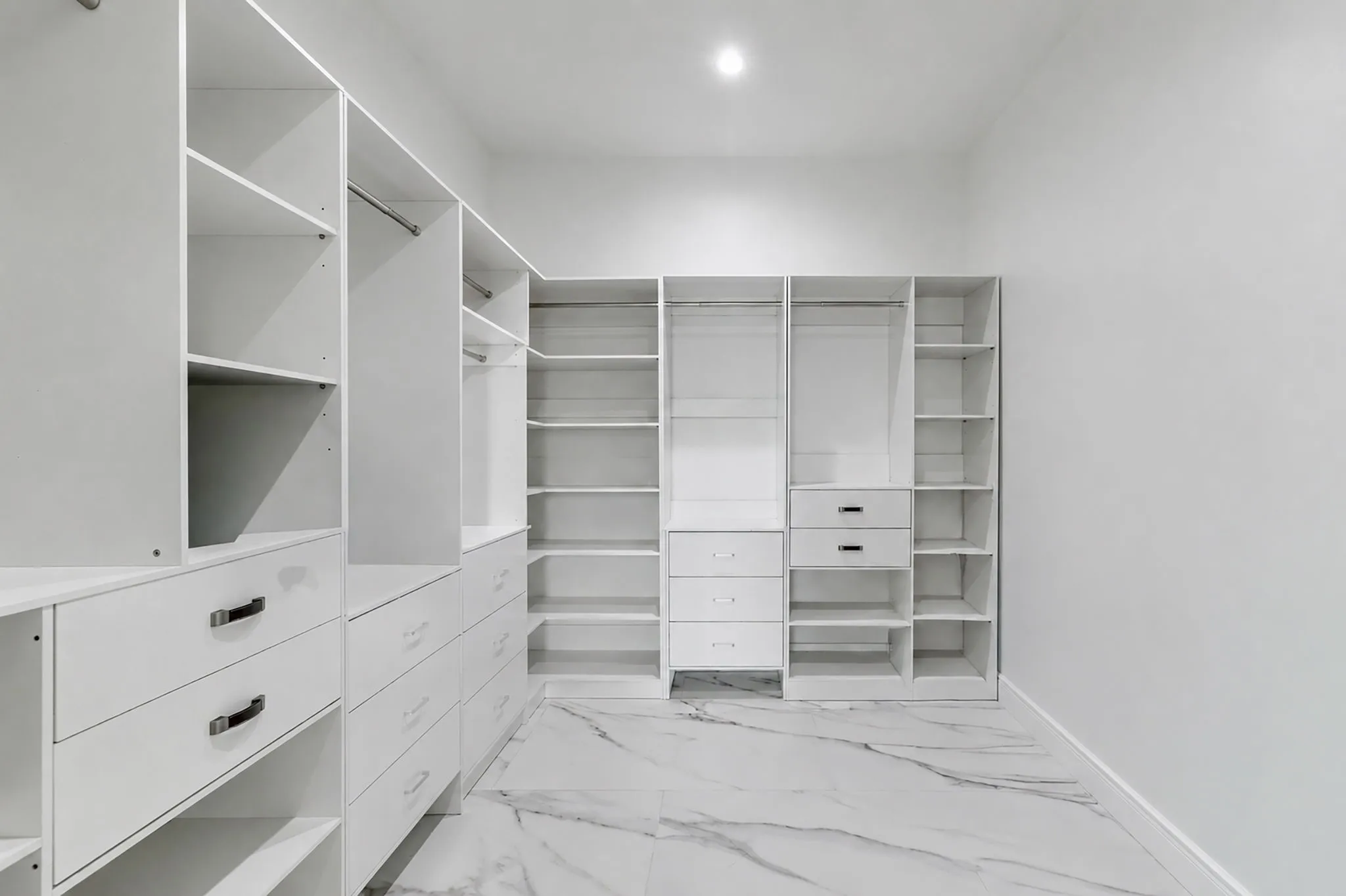 Expansive walk-in closet featuring white built-in shelving, multiple drawers, hanging rods, and large format marble-look tile flooring