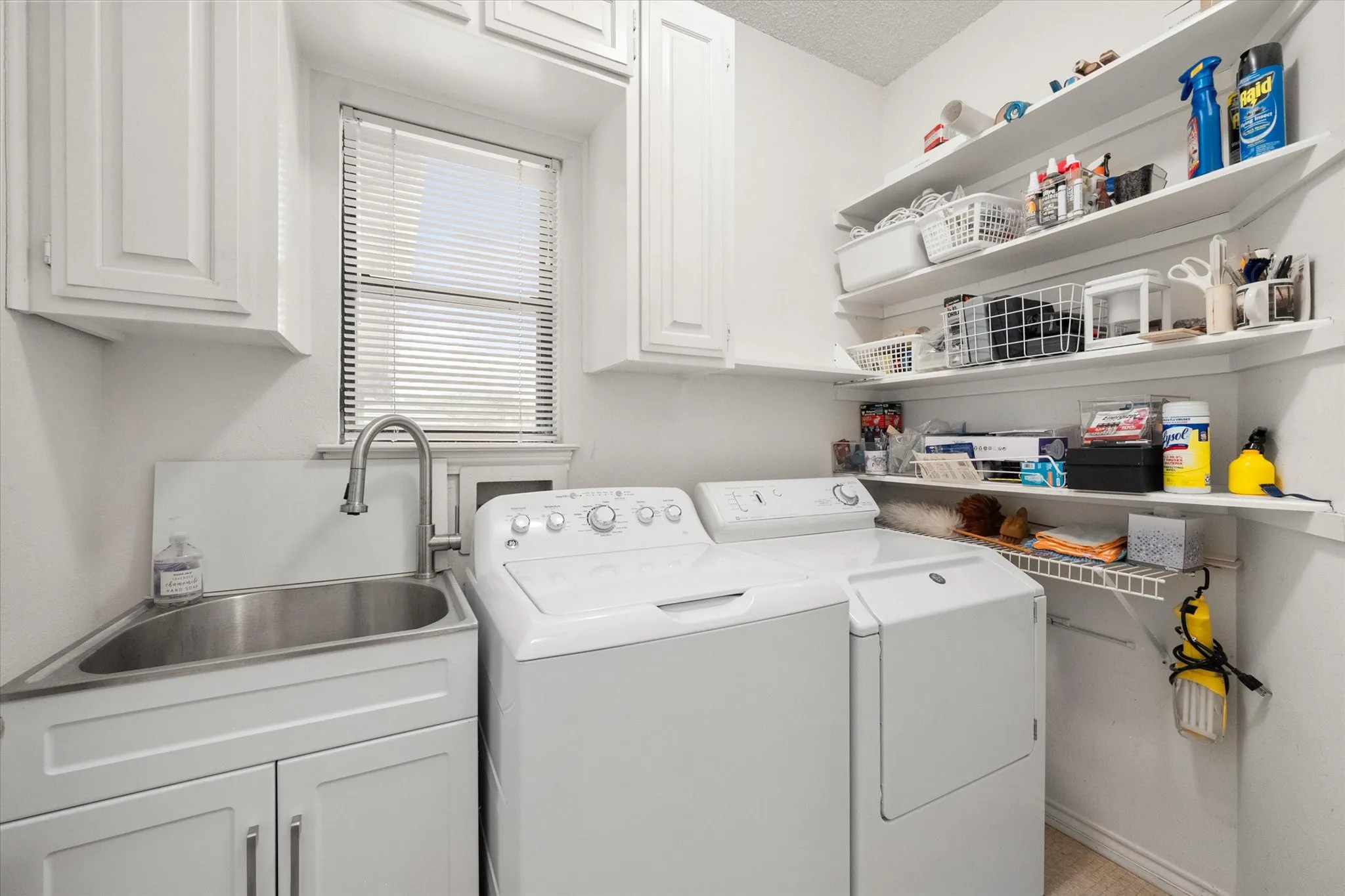 Dedicated laundry space featuring a utility sink with a gooseneck faucet, upper cabinetry, and open shelving for organization