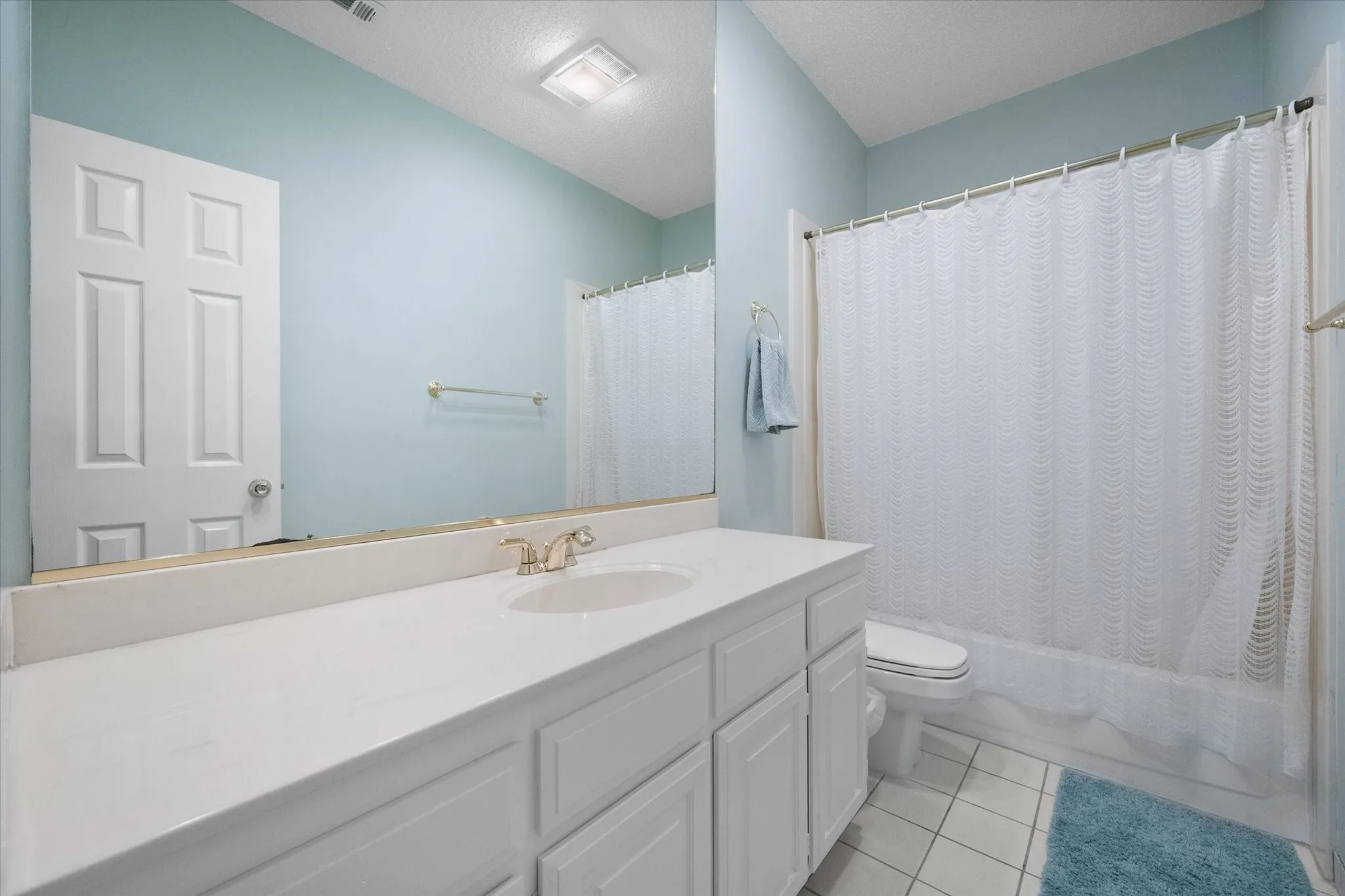 Bathroom featuring a white vanity with integrated sink, gold-toned faucet, large wall mirror, and a shower-tub combination with white tile surround