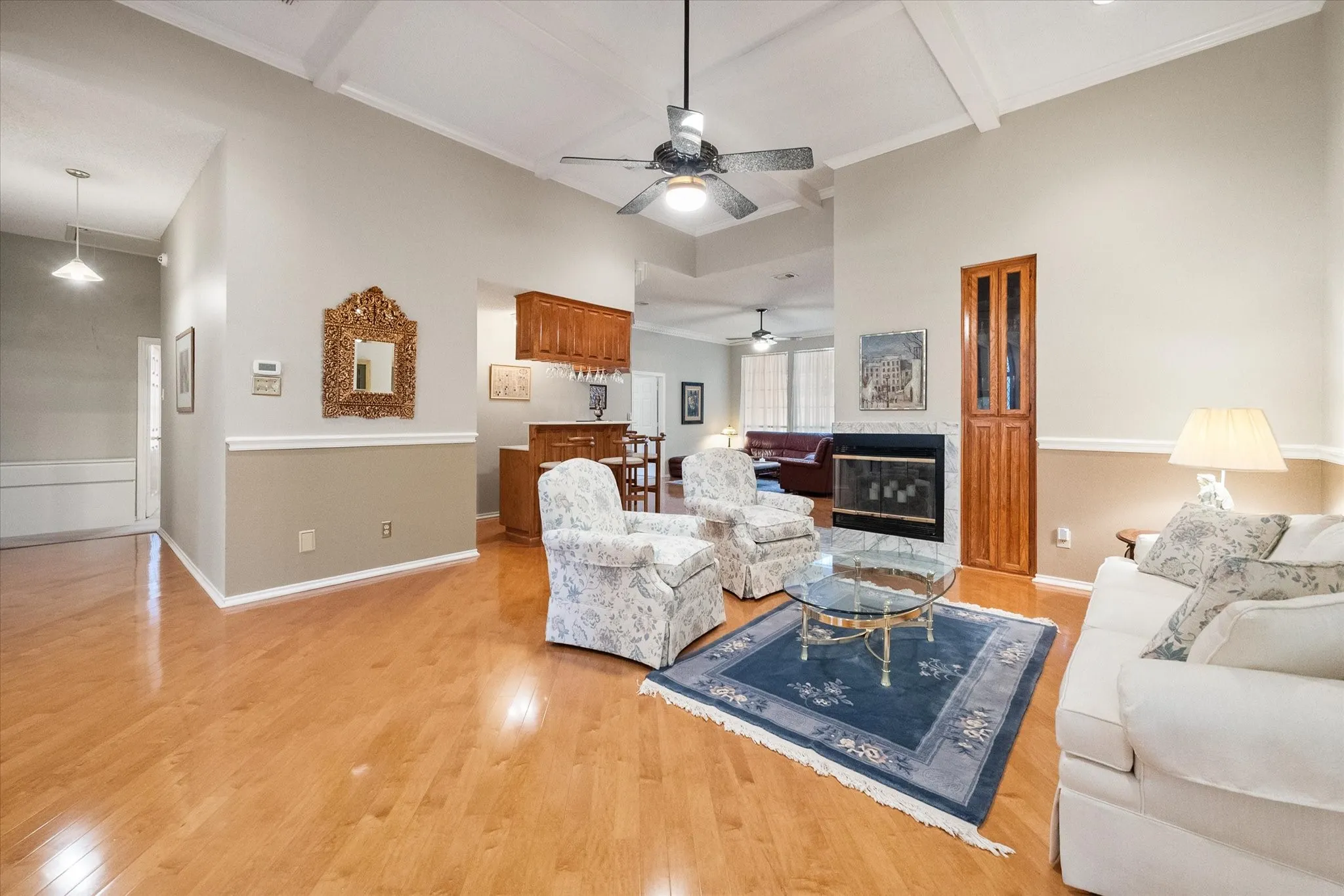 Spacious living area featuring high vaulted ceilings with exposed beams, wood-finish flooring, and a fireplace with a stone surround