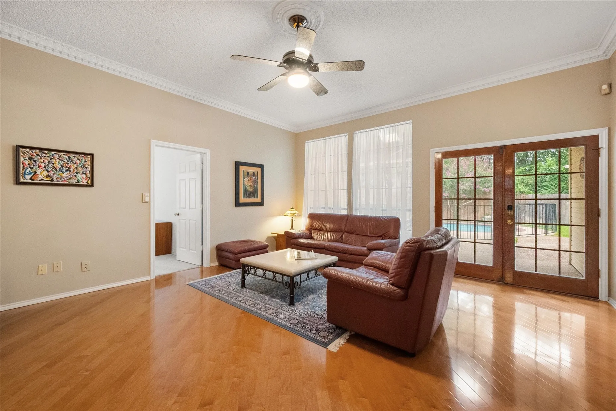 Hardwood-style flooring throughout, featuring crown molding, a ceiling fan, and large windows with privacy blinds